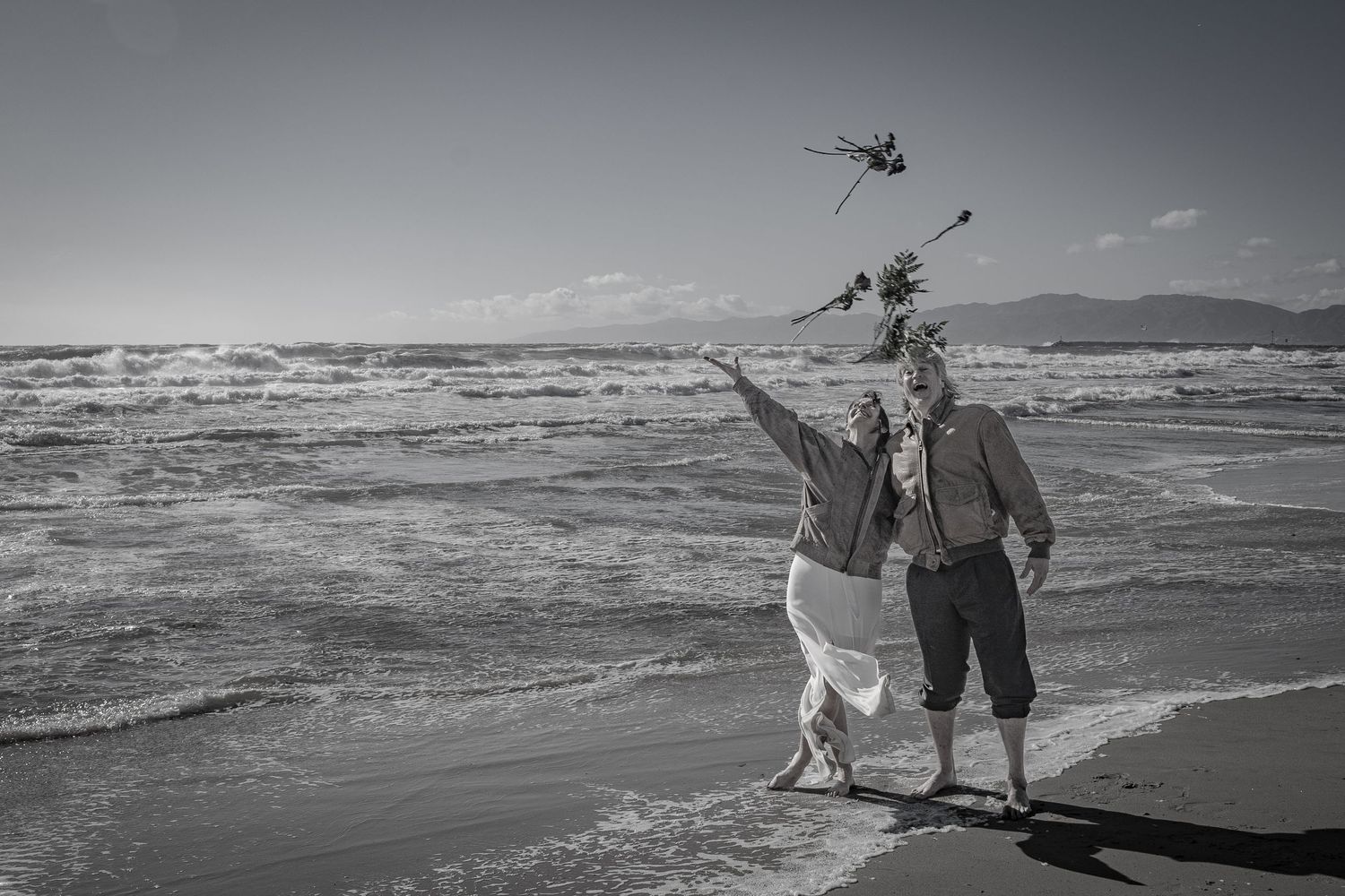 Happy wedding couple throws their bouquet in the air at the beach after renewing their vows on the beach in Playa del Rey, Los Angeles.