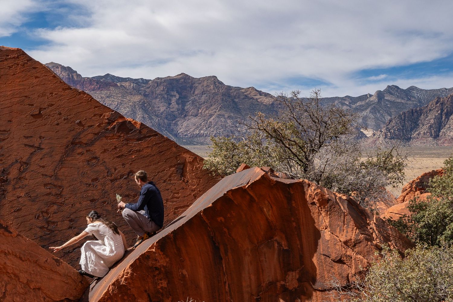 A couple climbing down rocks in their wedding clothes in Red Rocks, Nevada.