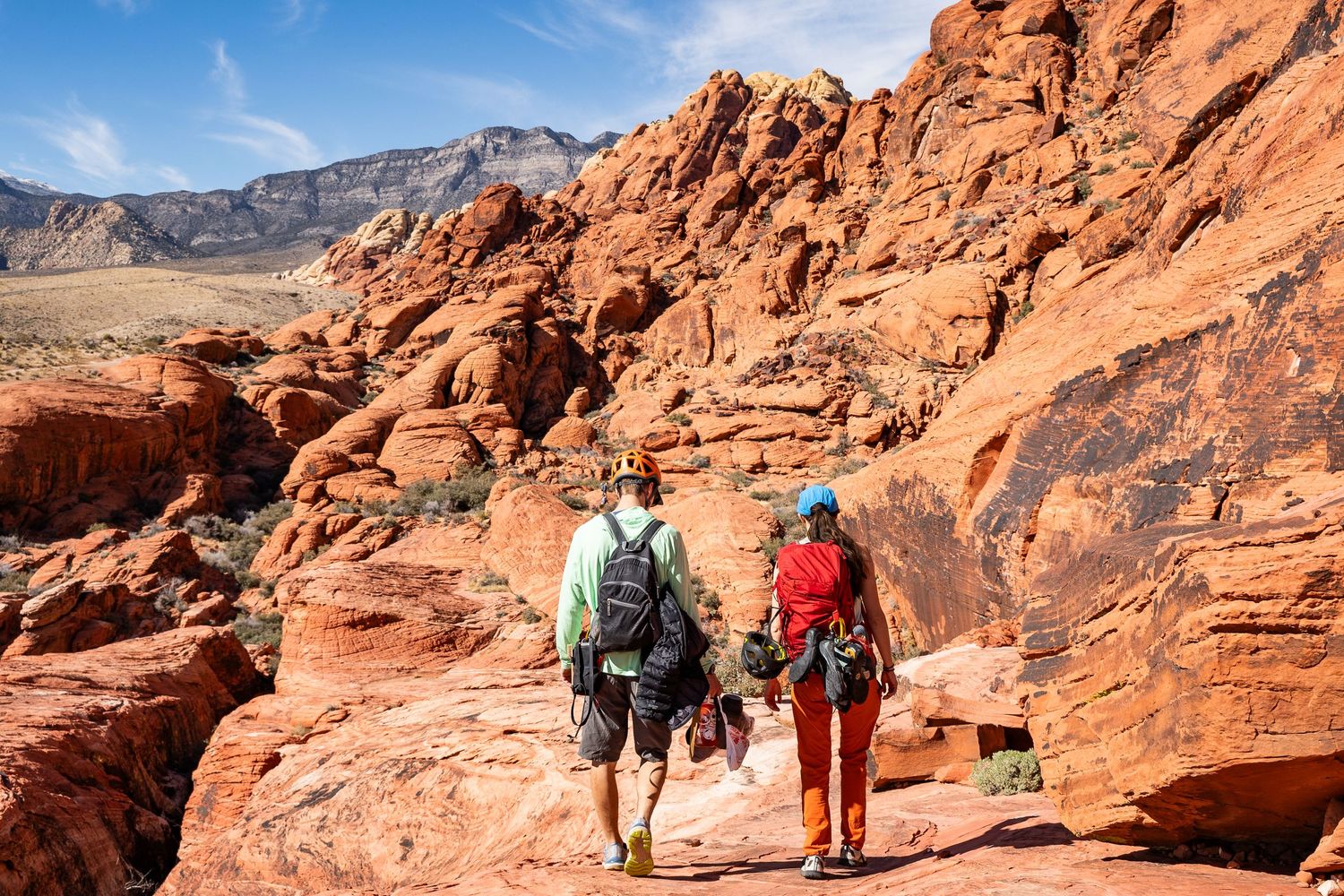 A couple walking with heavy climbing backpacks on their wedding day in Red Rocks, Nevada.