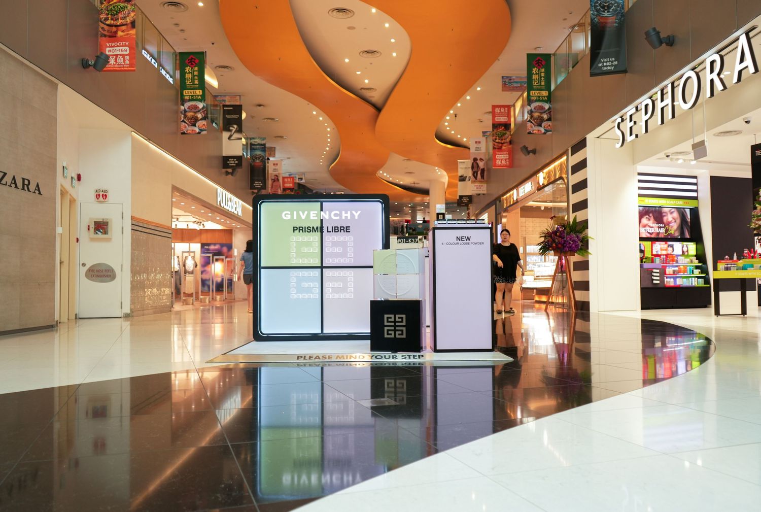 Sleek retail kiosk with digital displays under an orange curved ceiling in a shopping mall.