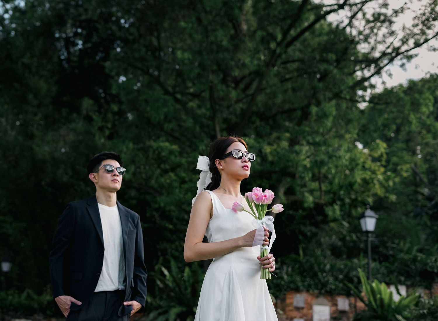 Wedding couple poses in garden setting with bride holding pink flowers.