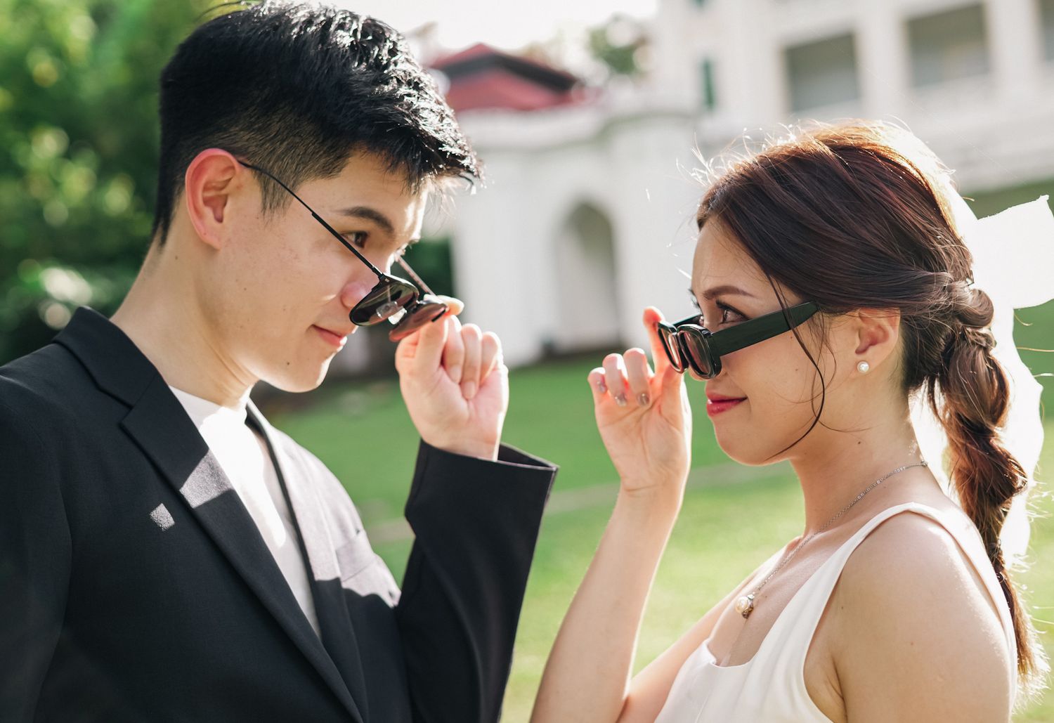 Stylish couple in formal wear adjusting their sunglasses outdoors.