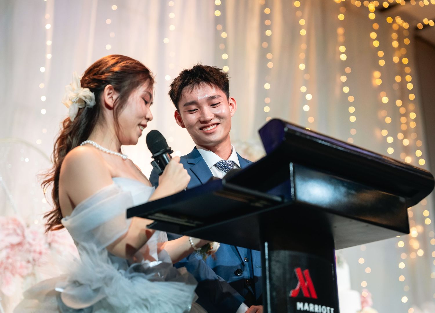 A couple shares a romantic moment at a piano with twinkling string lights creating an intimate ambiance in the background.