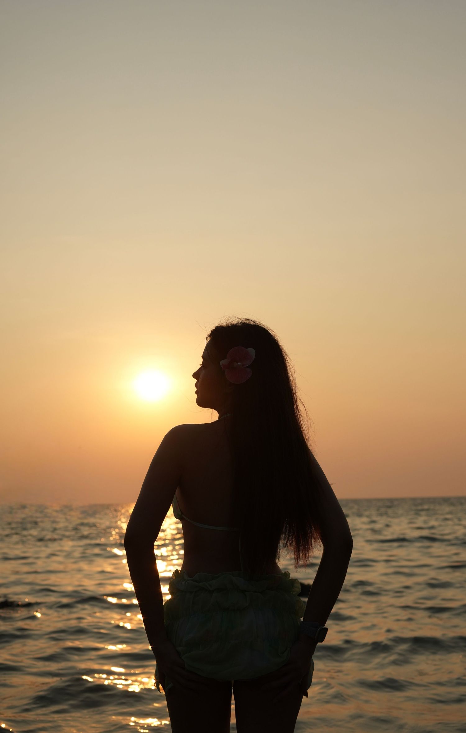 Silhouette of person sitting by ocean at sunset with golden light reflecting on calm waters.