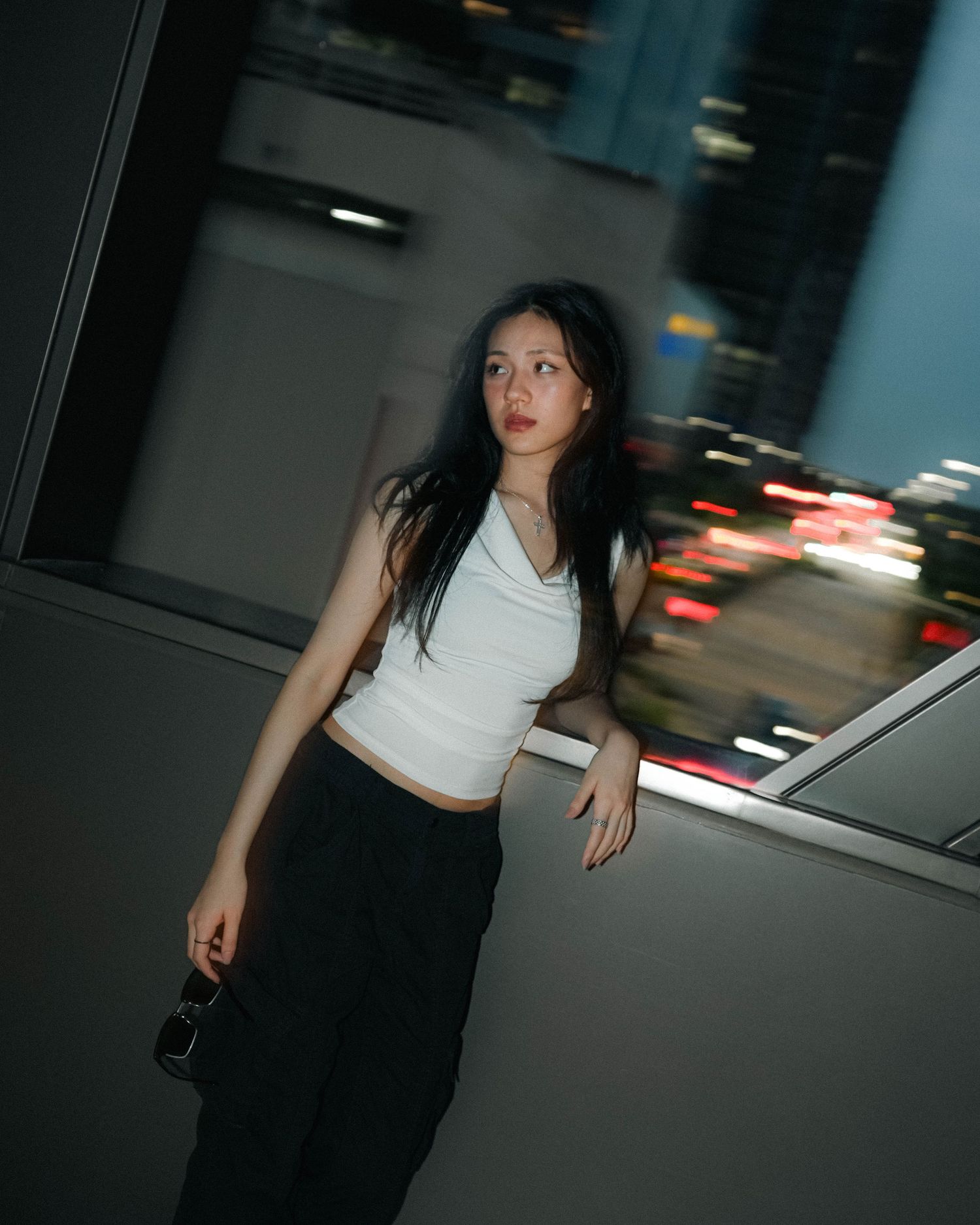 A person in a white crop top and dark pants stands against a blurred cityscape background with motion blur effects at night.