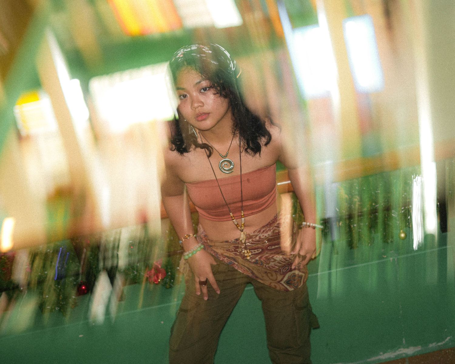 Young woman in orange top posing expressively against green background with motion blur effect.