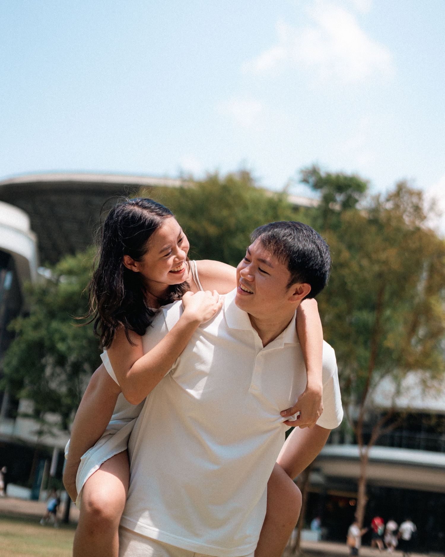 Playful couple enjoying piggyback ride outdoors on sunny day.