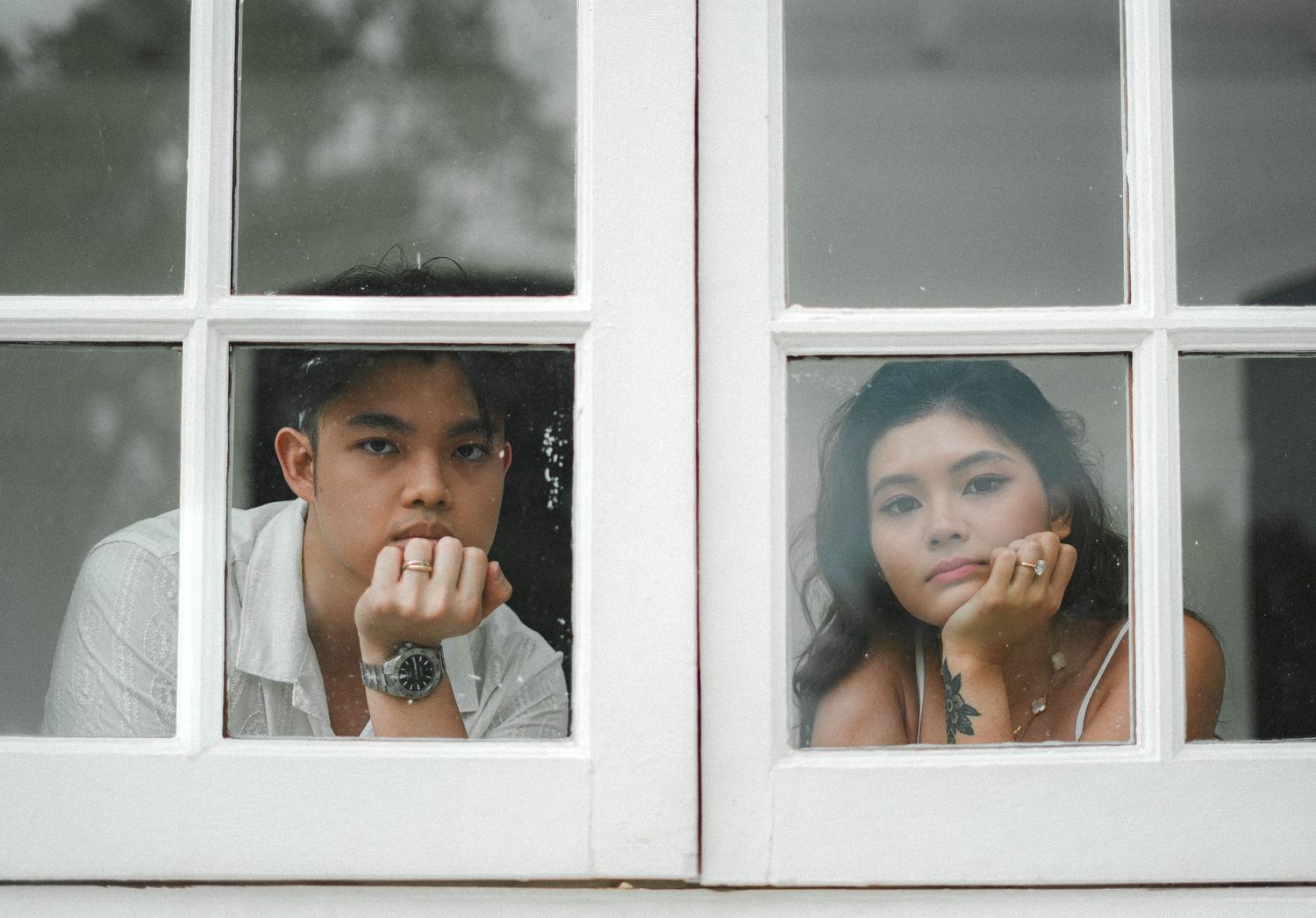 Two people gazing dreamily through separate window panes with chins resting on hands.