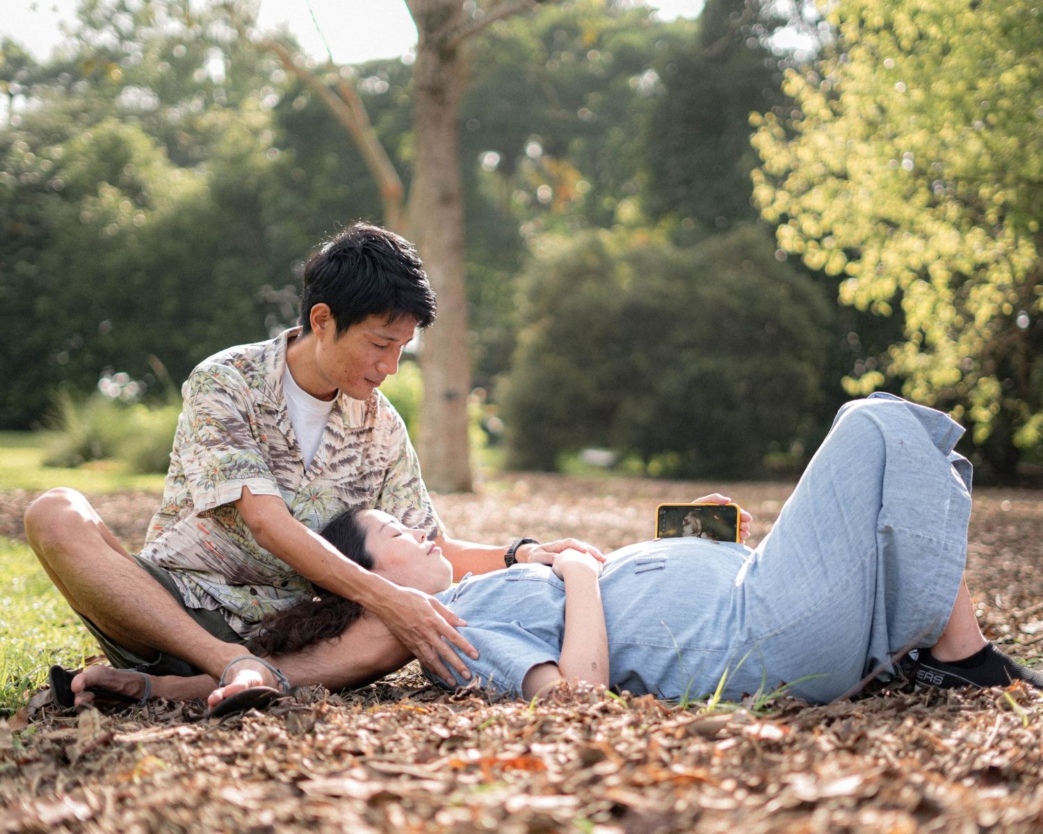 Two people relaxing together on fallen leaves in park during autumn.