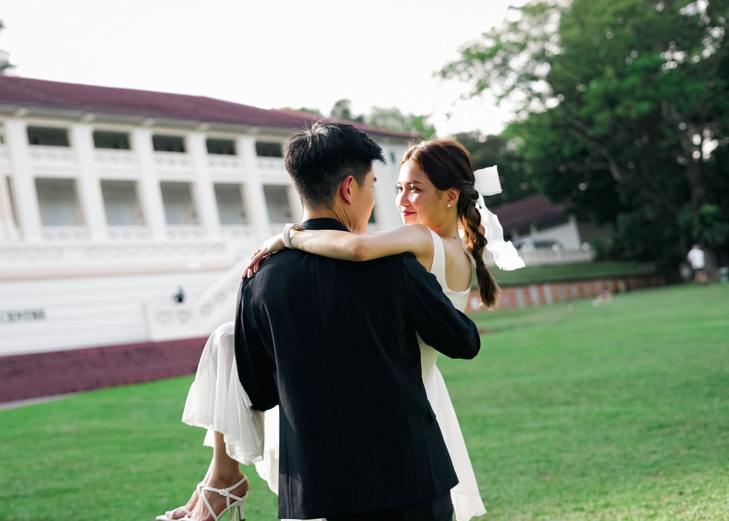 A romantic couple shares an intimate dance moment on a grassy lawn in front of a colonial-style building.