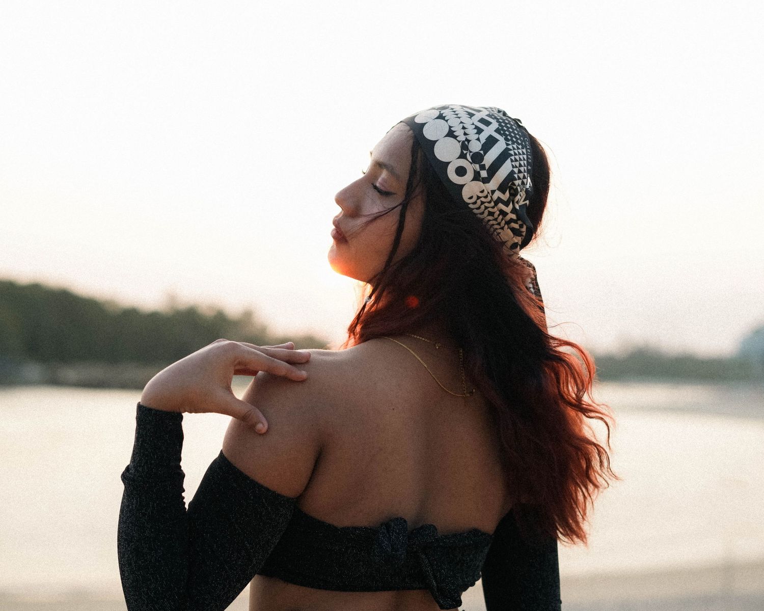 Sunset silhouette portrait with ornate headpiece against waterfront background.