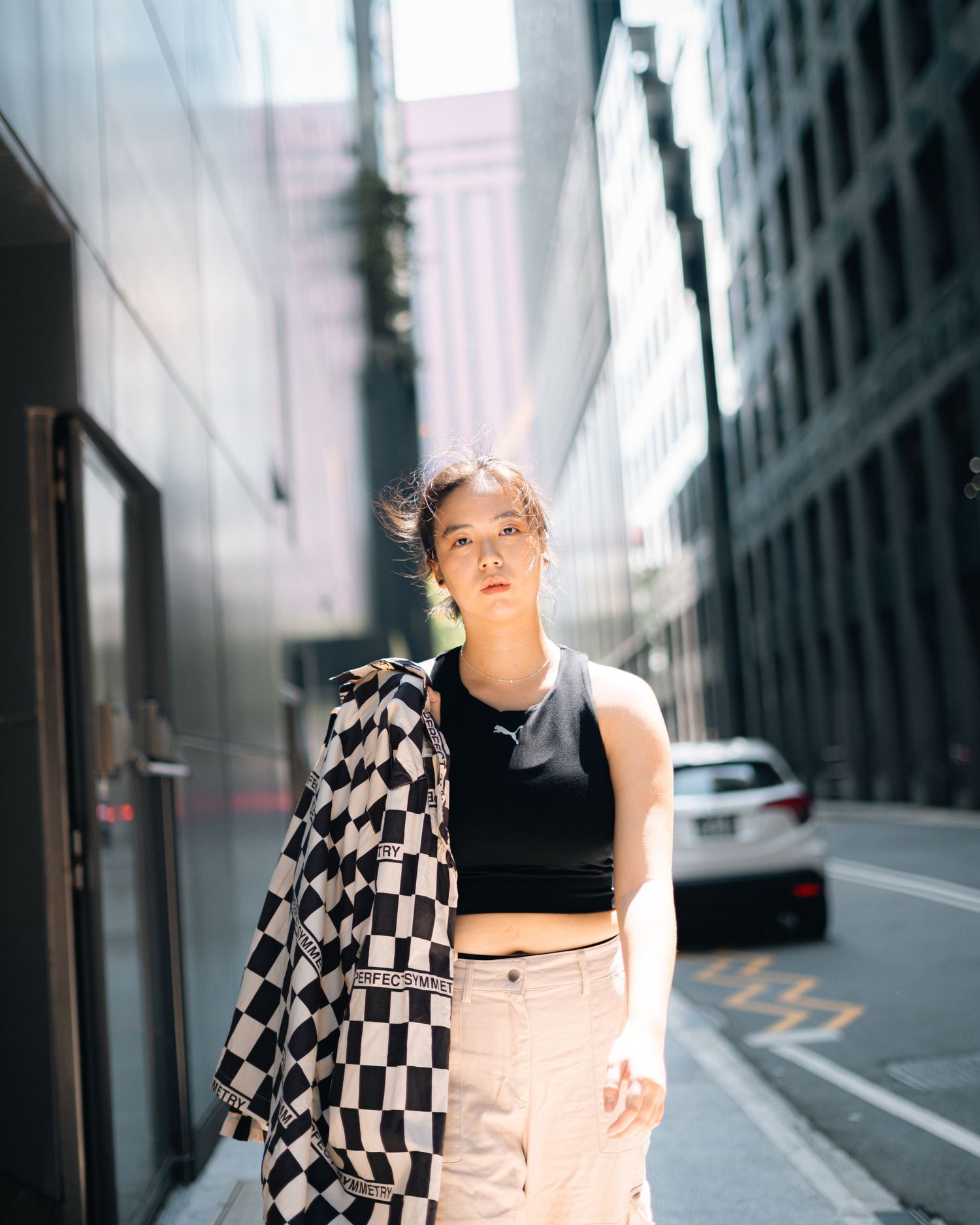 Urban street fashion with checkered jacket against city buildings backdrop.