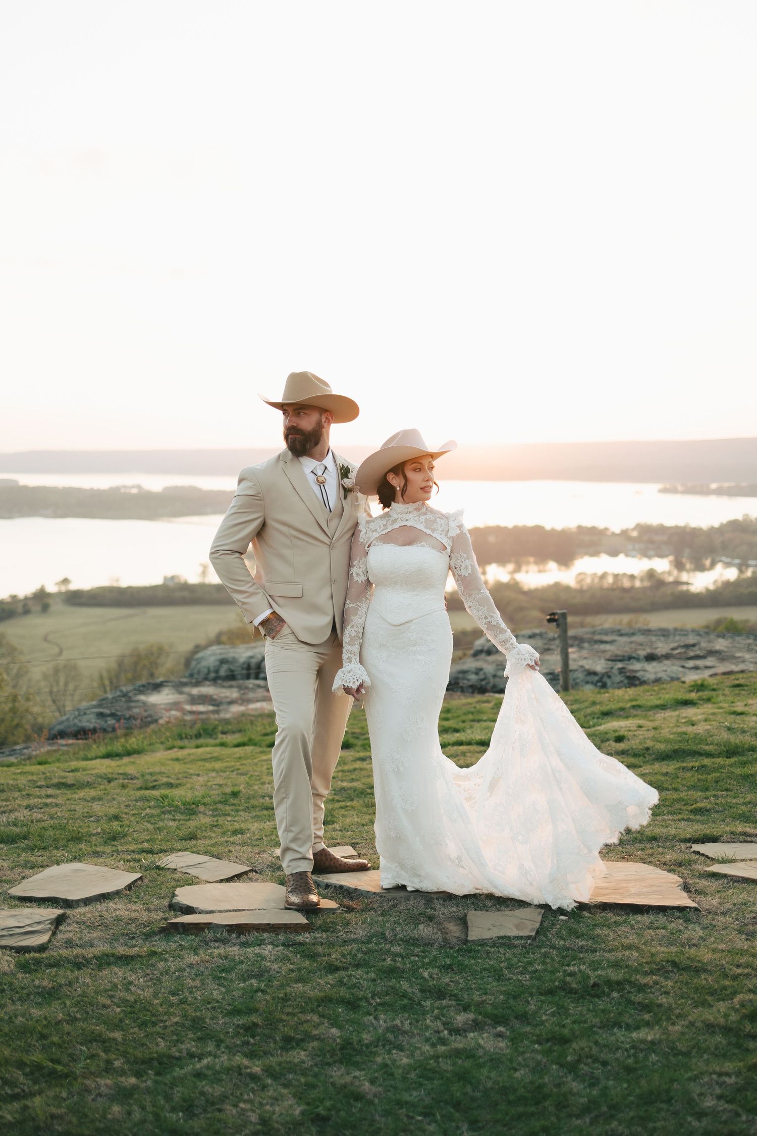 Western-style wedding couple in cowboy hats posing at sunset overlooking a scenic lake.