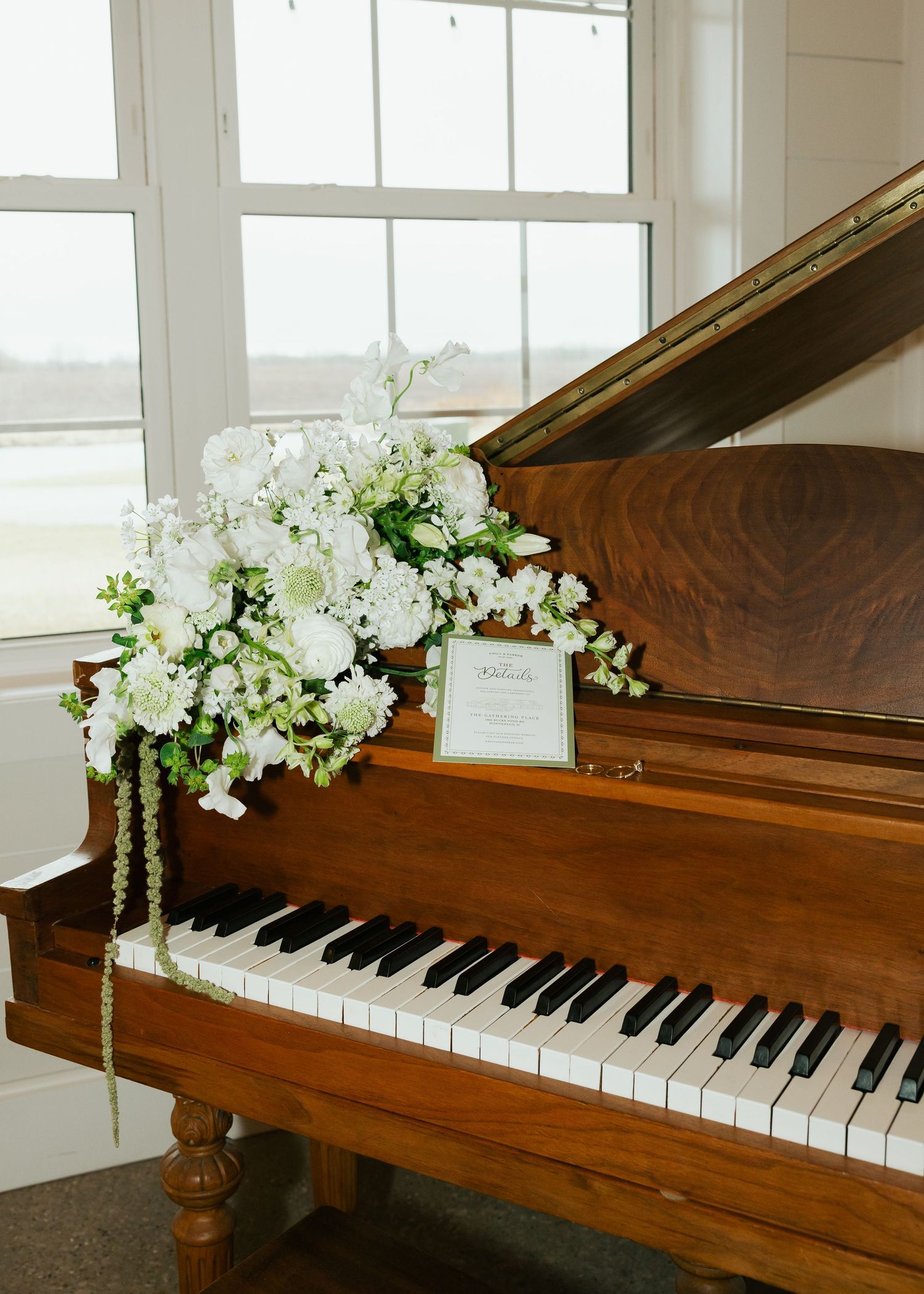 White floral arrangement with cascading greenery decorating a wooden grand piano.