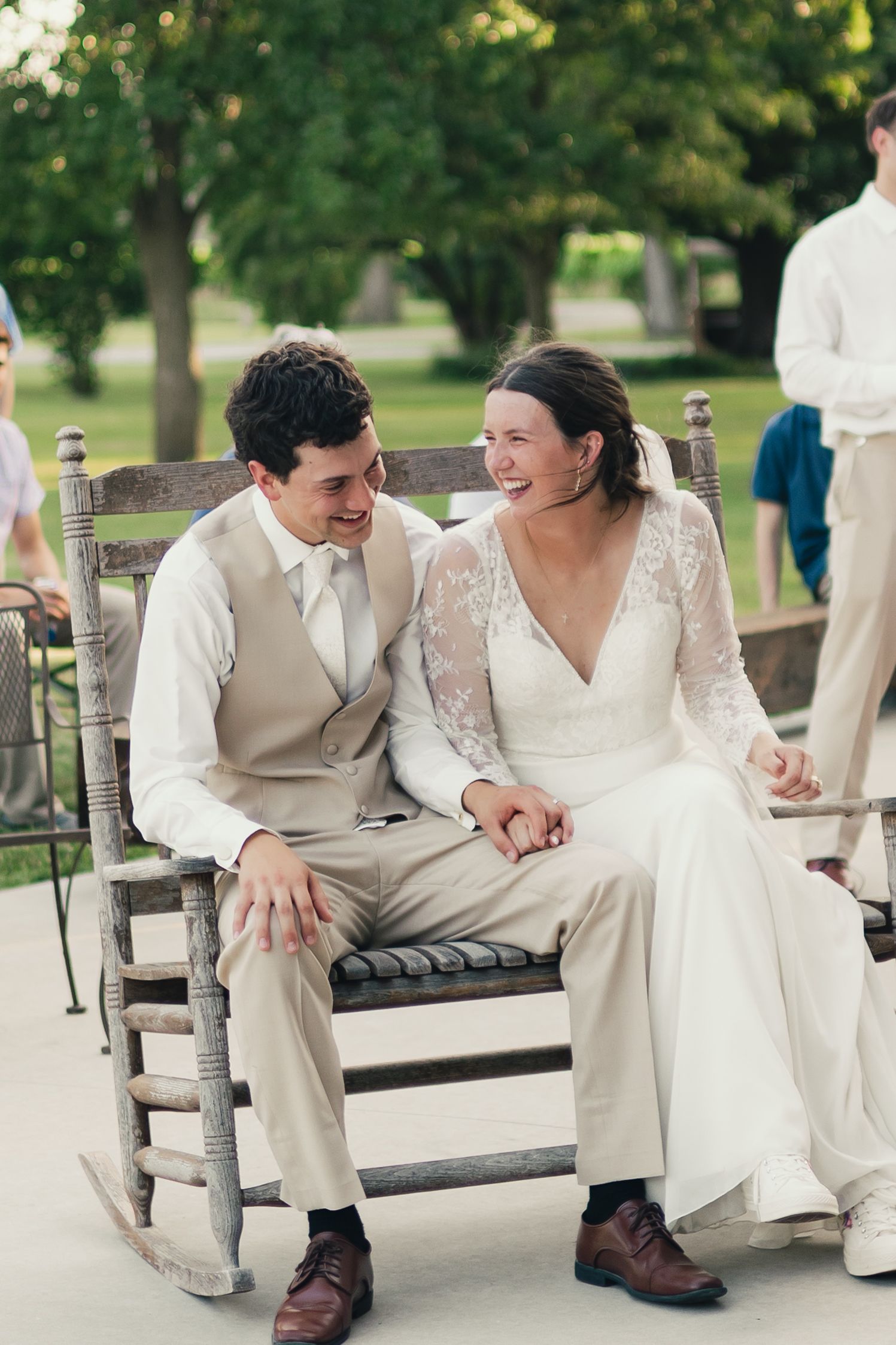 Happy bride and groom sitting together in rustic rocking chairs laughing during outdoor wedding reception.