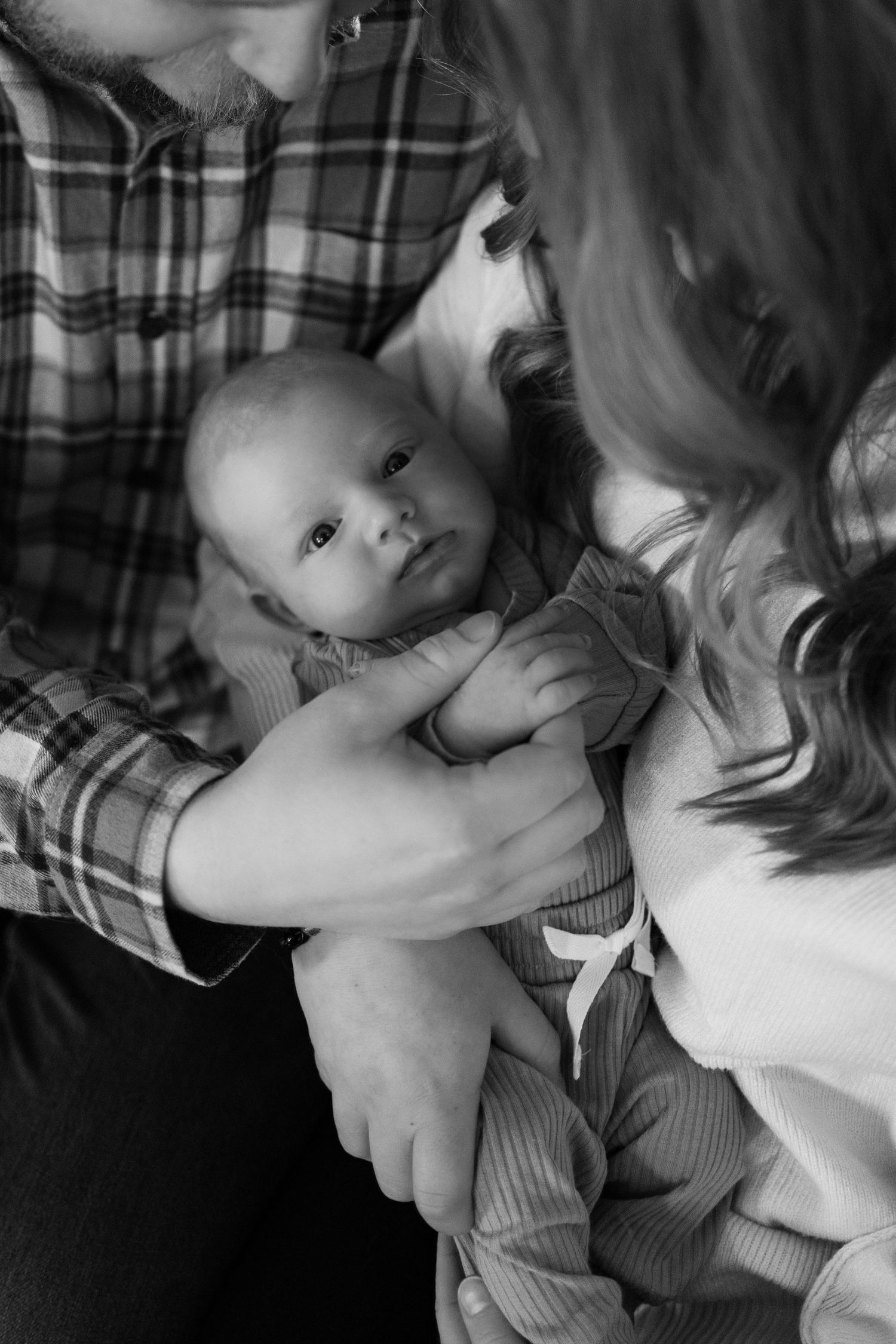Black and white close-up of new parents tenderly cradling their newborn baby together.