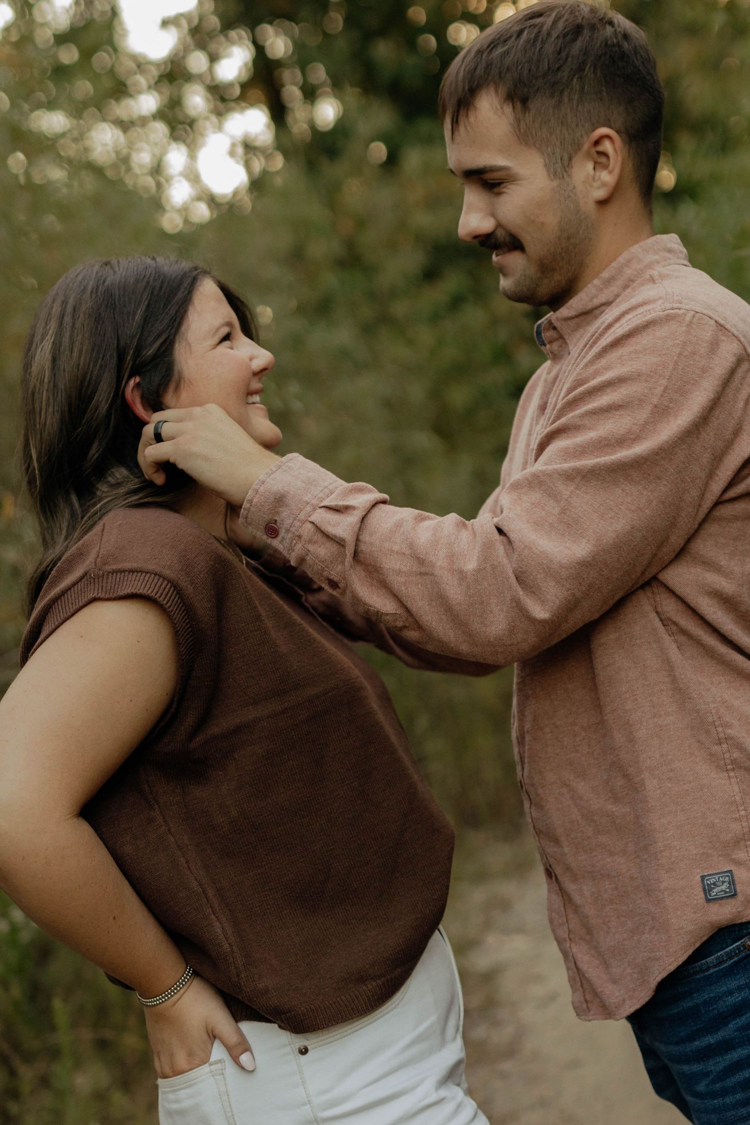 Couple sharing tender moment outdoors, man gently touching womans face in nature.
