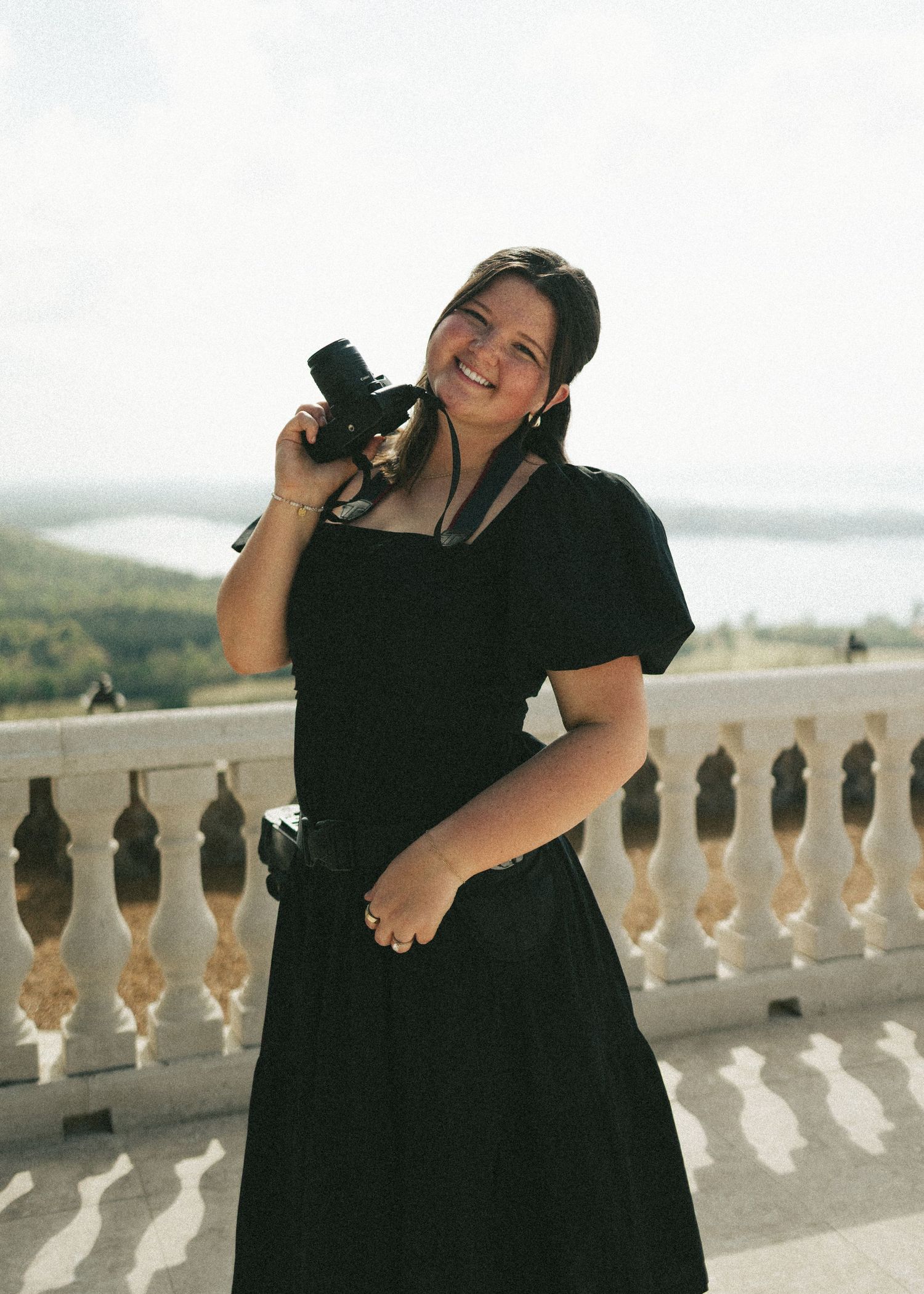 Alabama photographer in black dress holding a camera on a sunlit scenic overlook.