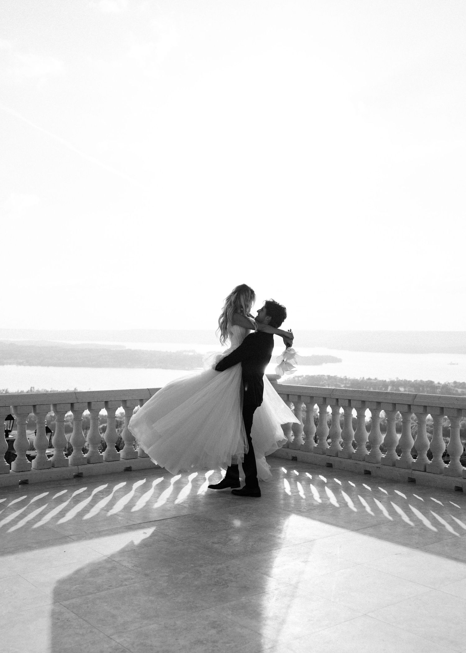 Groom lifting bride in a romantic black and white photo on a scenic balcony.