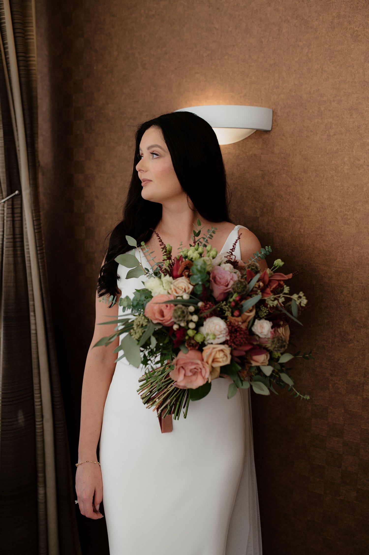 Beautiful floral arrangement with pink and white roses adorns a white wedding dress against a brown backdrop.