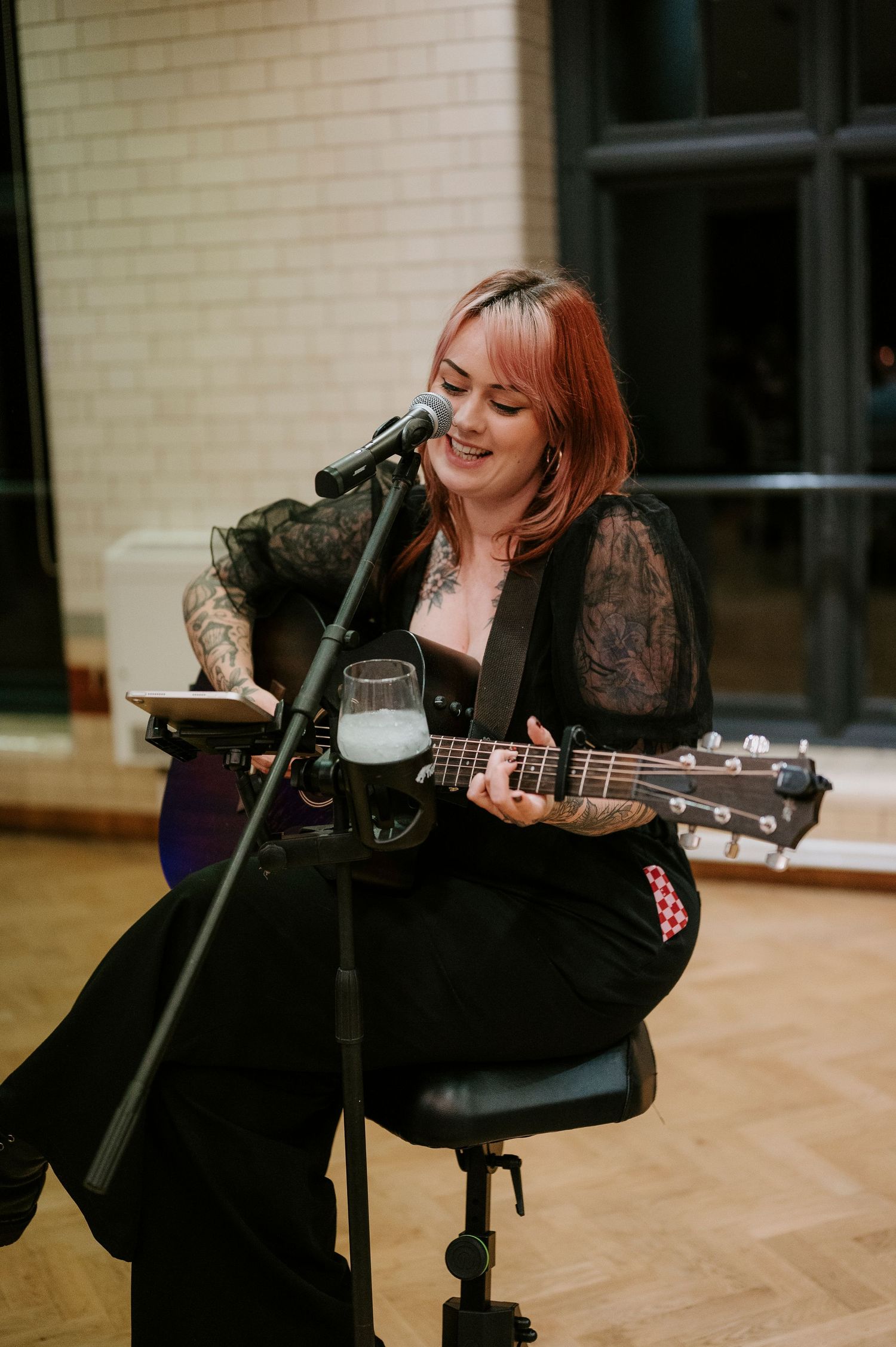 Musician performing with an acoustic guitar at an indoor event venue.