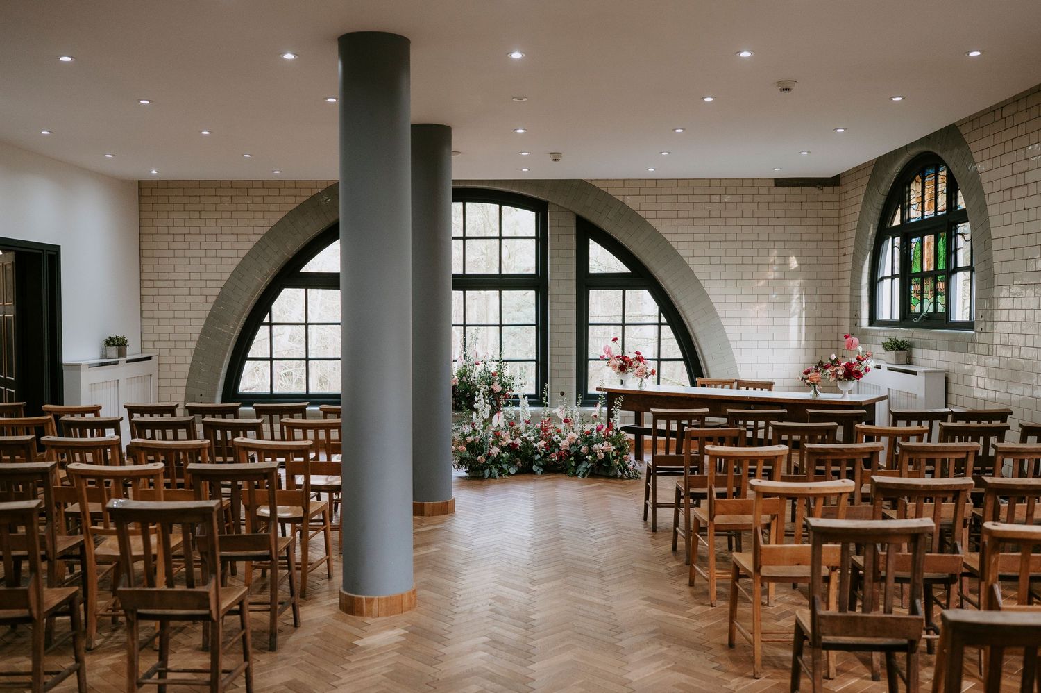Panoramic view of an empty wedding ceremony venue with wooden chairs arranged in rows under arched windows.
