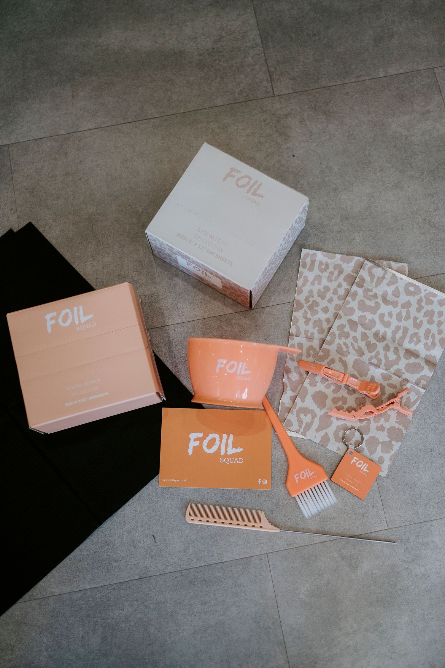 Flat lay of peach and white colored FOIL branded packaging boxes and accessories on concrete floor.