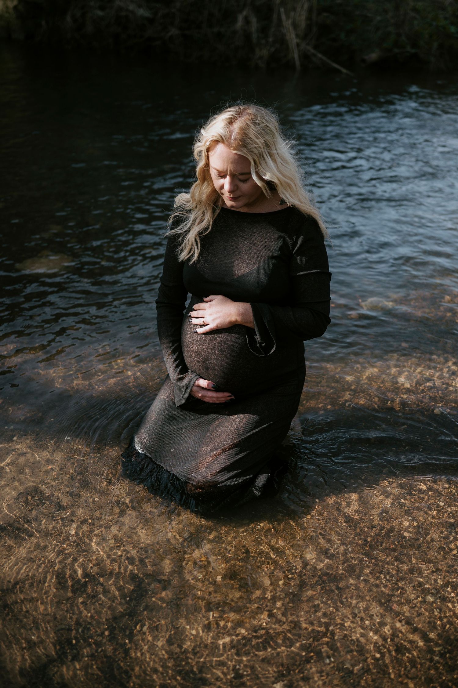 A figure in black sits contemplatively on rocks by dark water in a moody artistic photo series.
