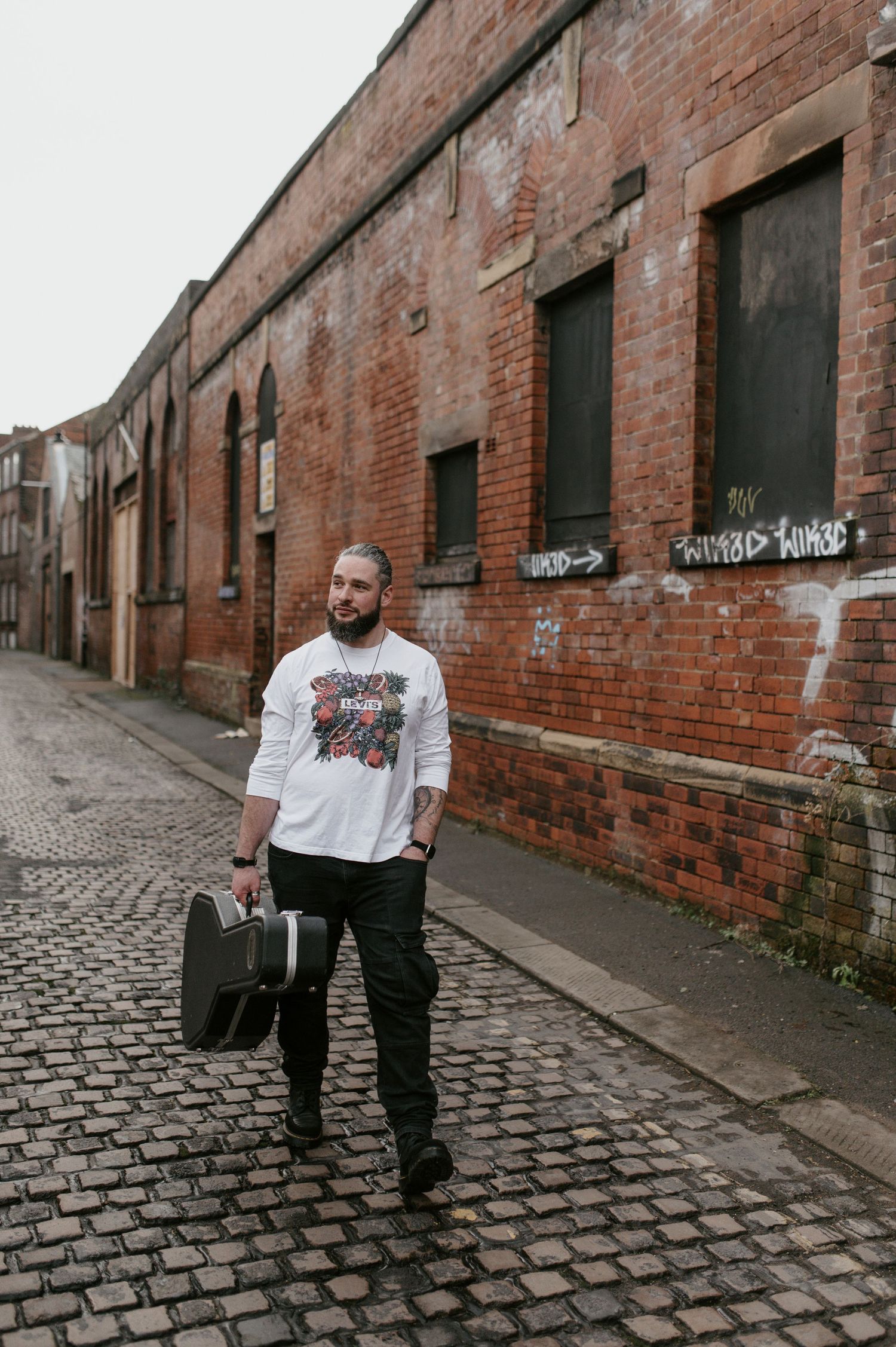 Person walks along cobblestone alley beside historic red brick industrial buildings.