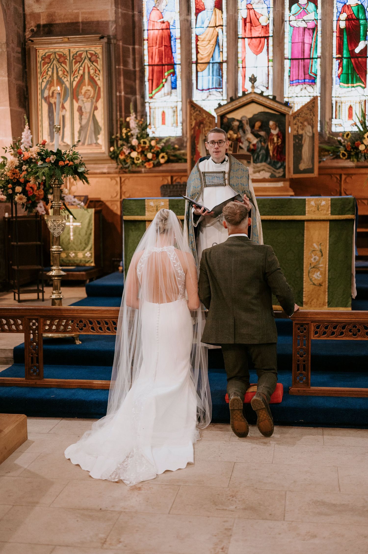 A couple stands together in a church sanctuary decorated with stained glass windows and floral arrangements for their wedding ceremony.
