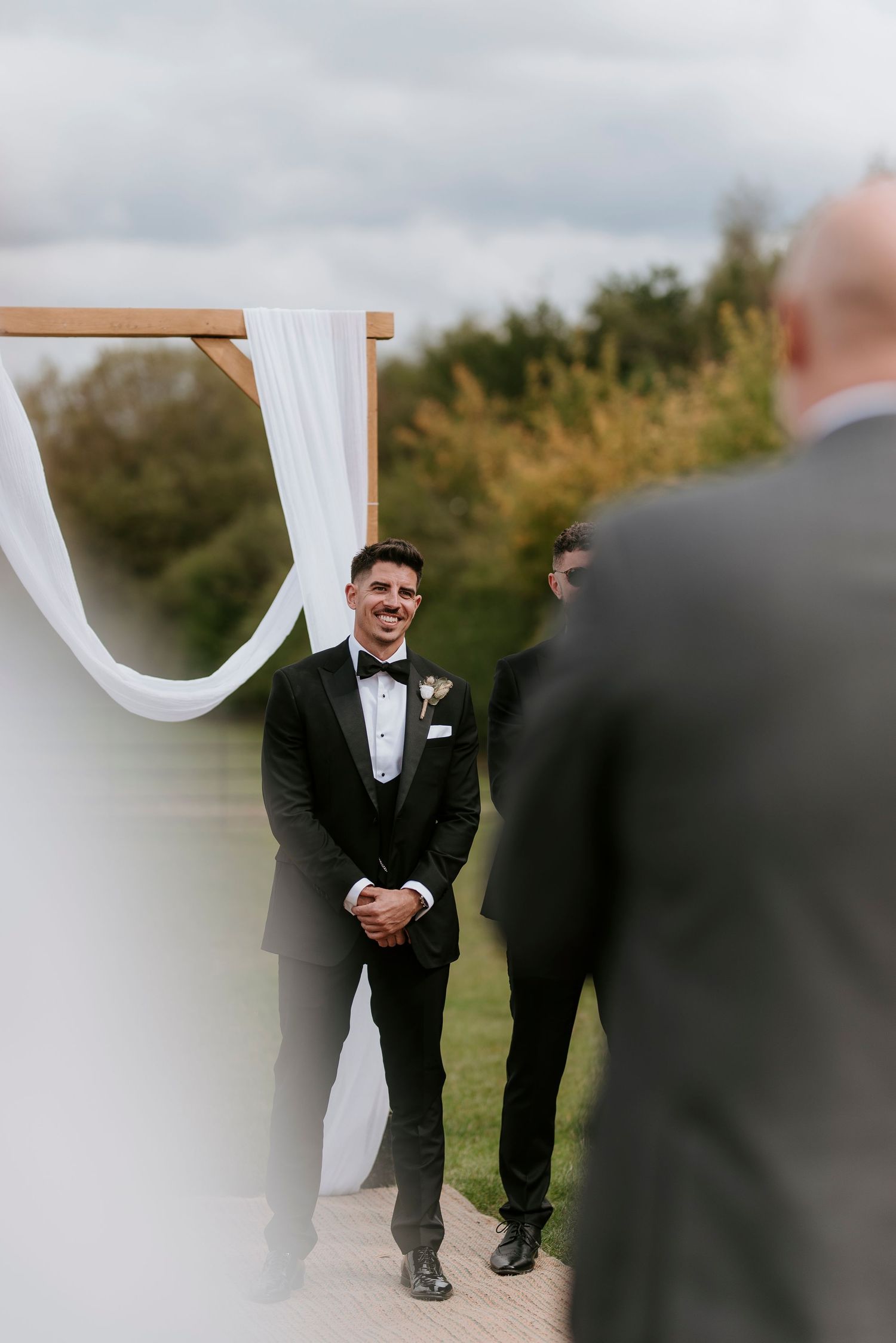 A candid moment captured at an outdoor wedding ceremony with white fabric draping and guests in formal attire.