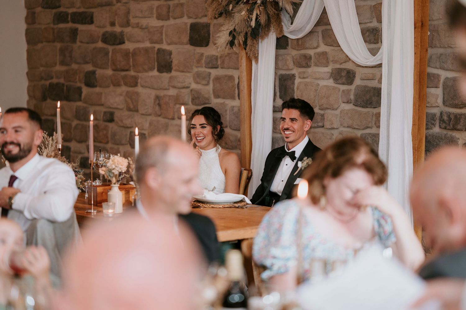 Wedding guests seated at long tables in a rustic brick venue during a reception celebration.