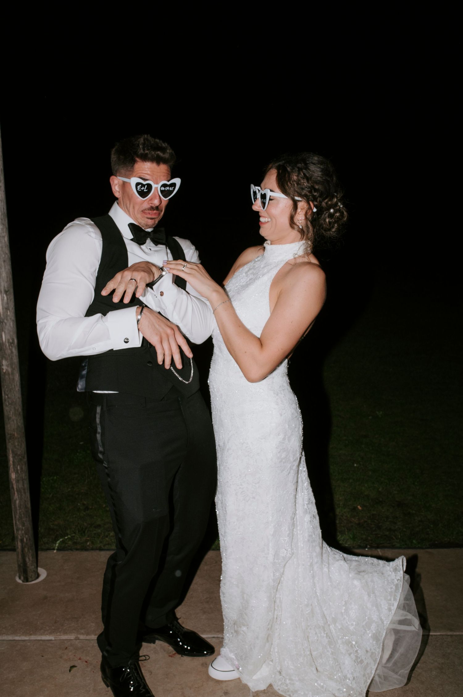 A couple in wedding attire dances together at night, with the bride wearing white and the groom in a dark suit.