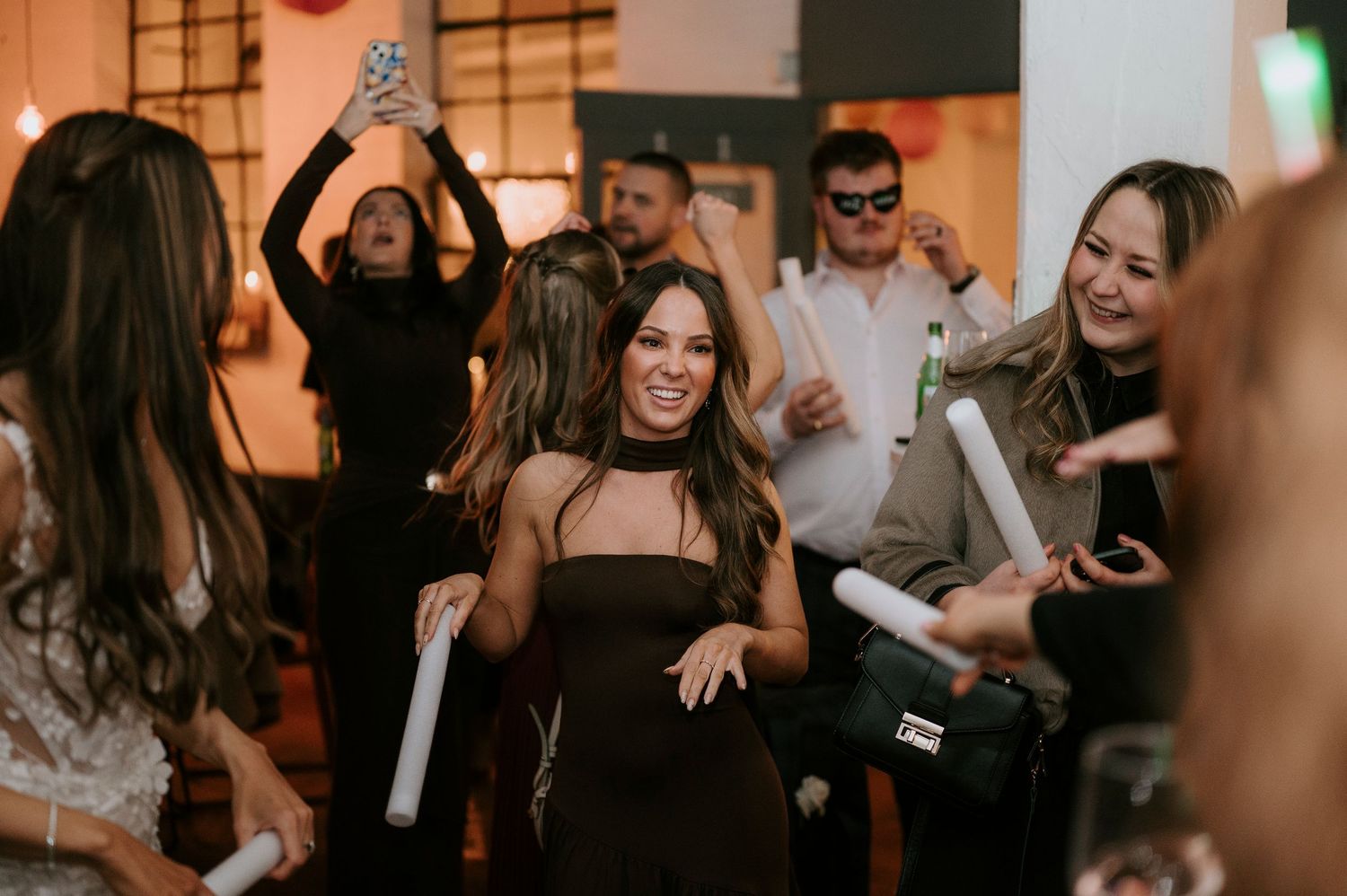 Guests dancing and celebrating at a lively party event, woman in black dress smiling in the center.