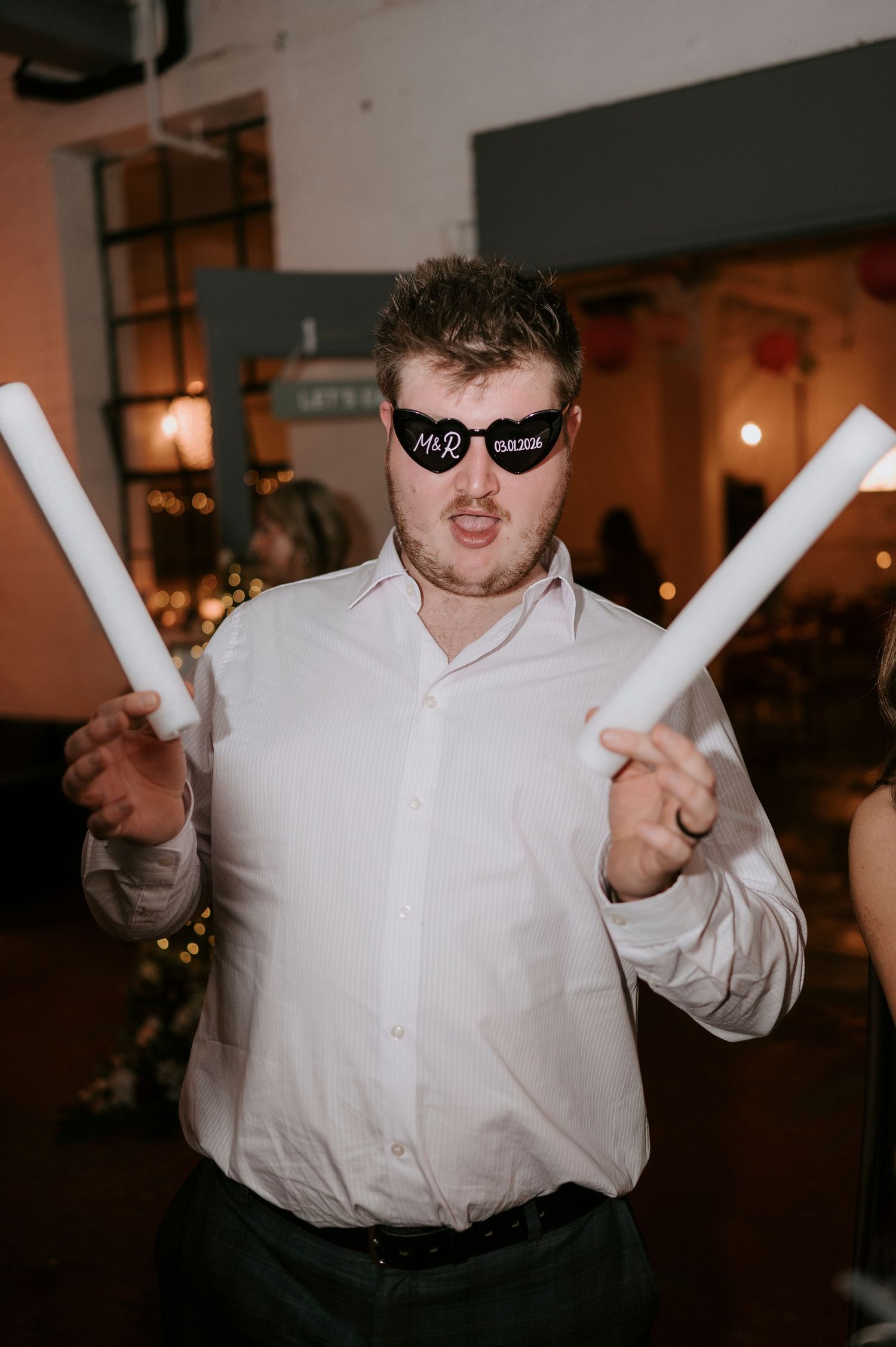 Wedding guest wearing Mr & Mrs novelty sunglasses holding foam sticks at lively wedding reception.