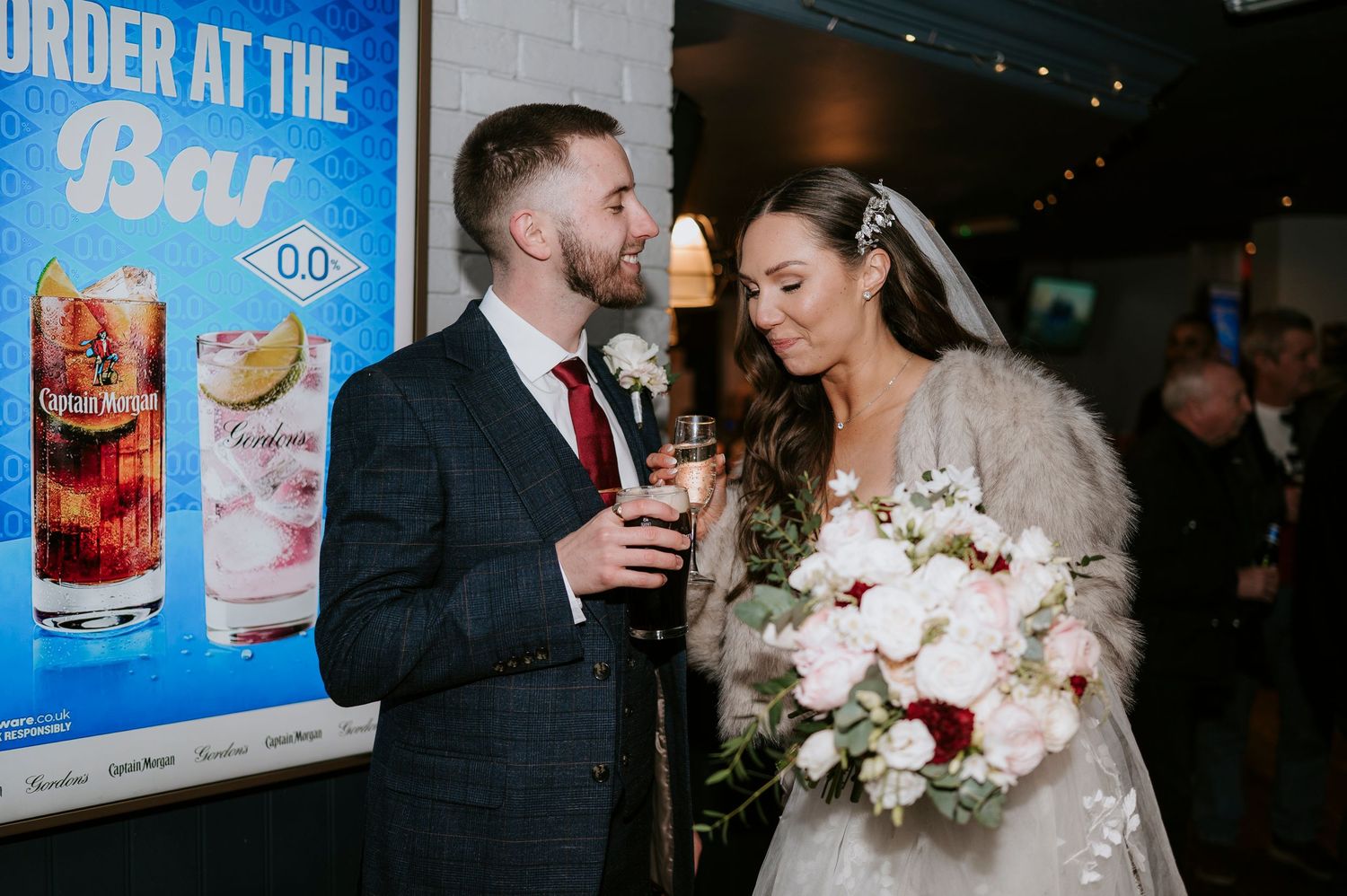 Bride and groom toasting with drinks at wedding reception, bride holding white floral bouquet wearing fur stole.