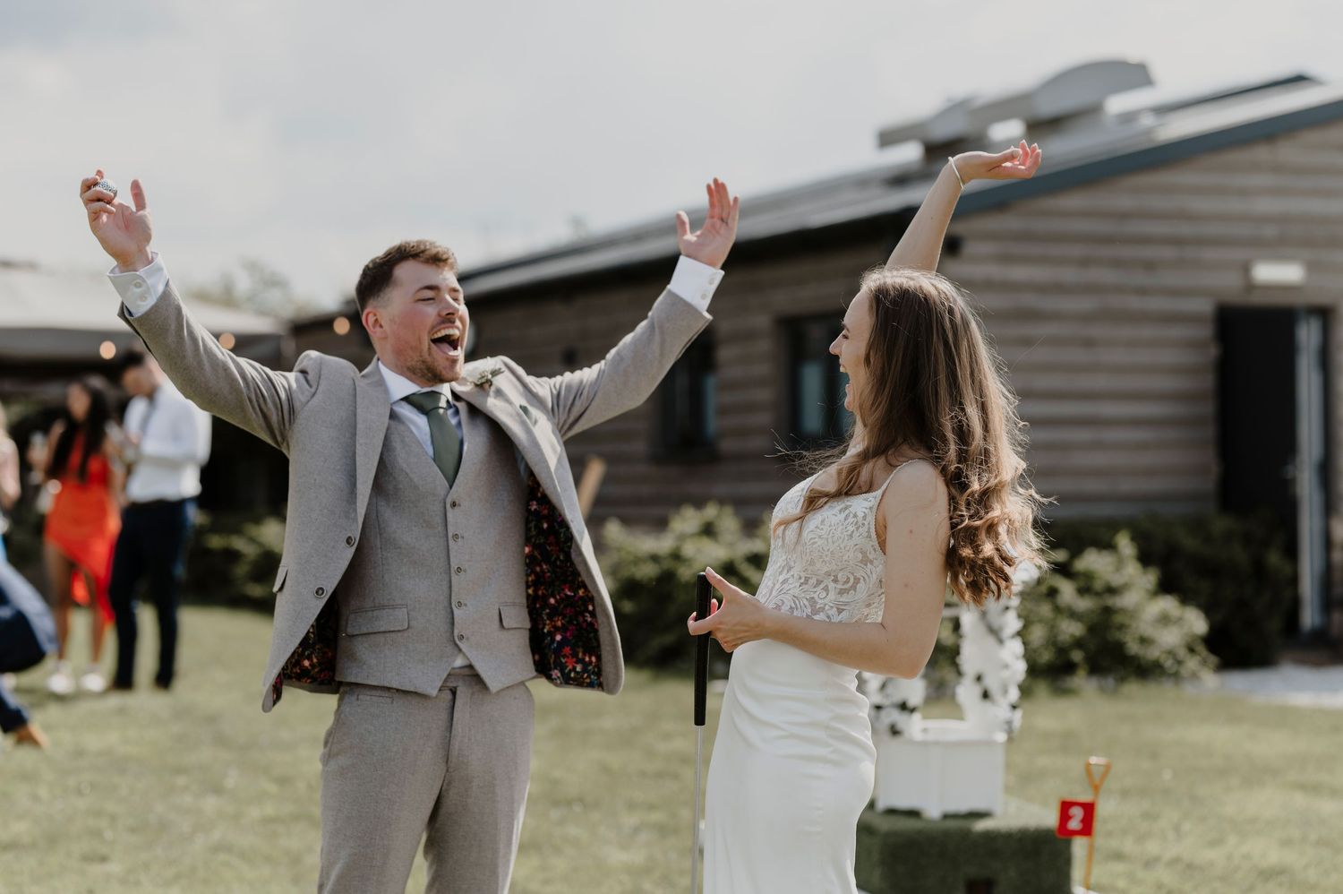 Joyful wedding celebration on a sunny lawn with modern buildings in background.