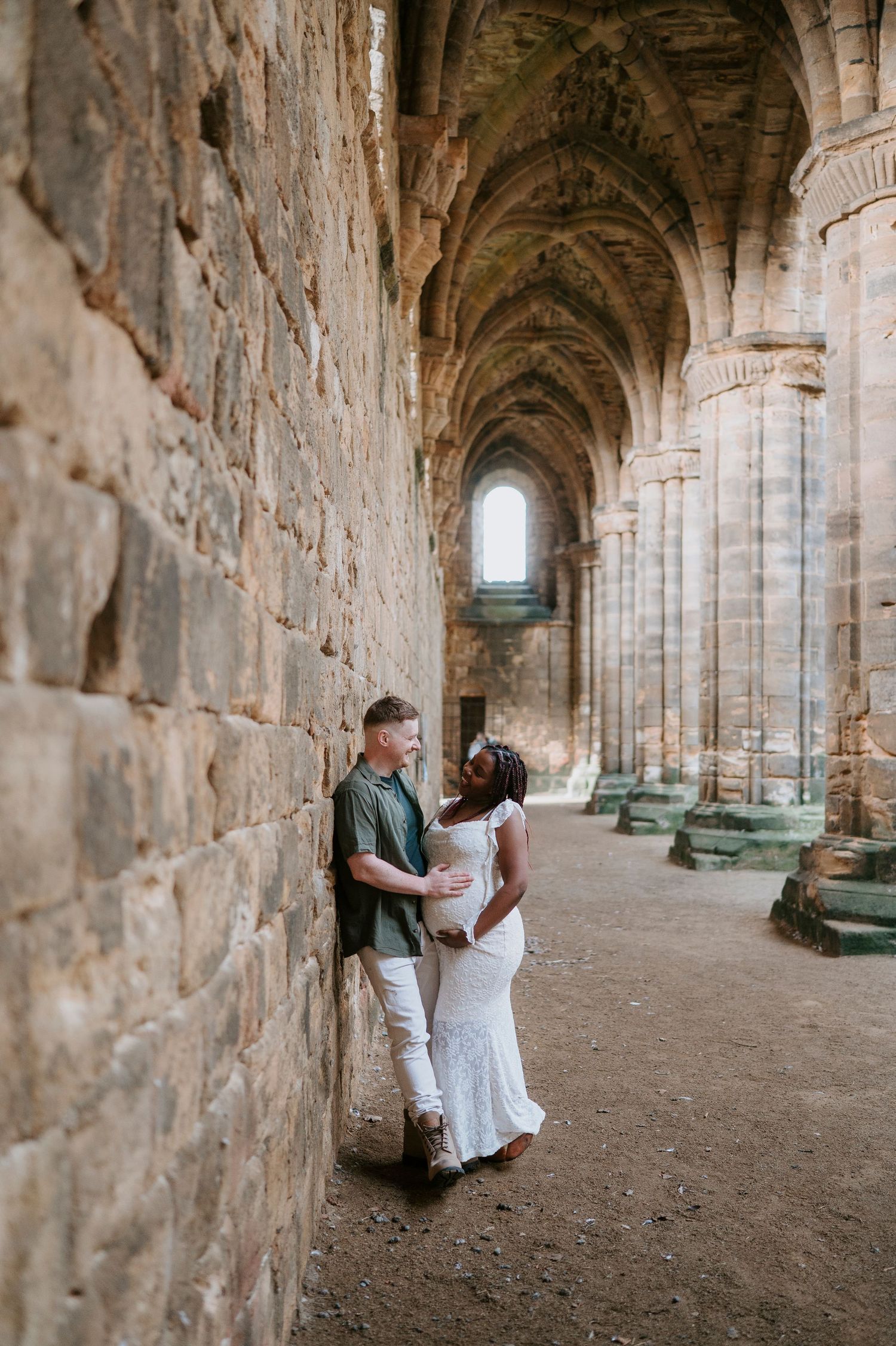 A couple shares romantic moments in a historic stone archway corridor of an ancient monastery or castle.