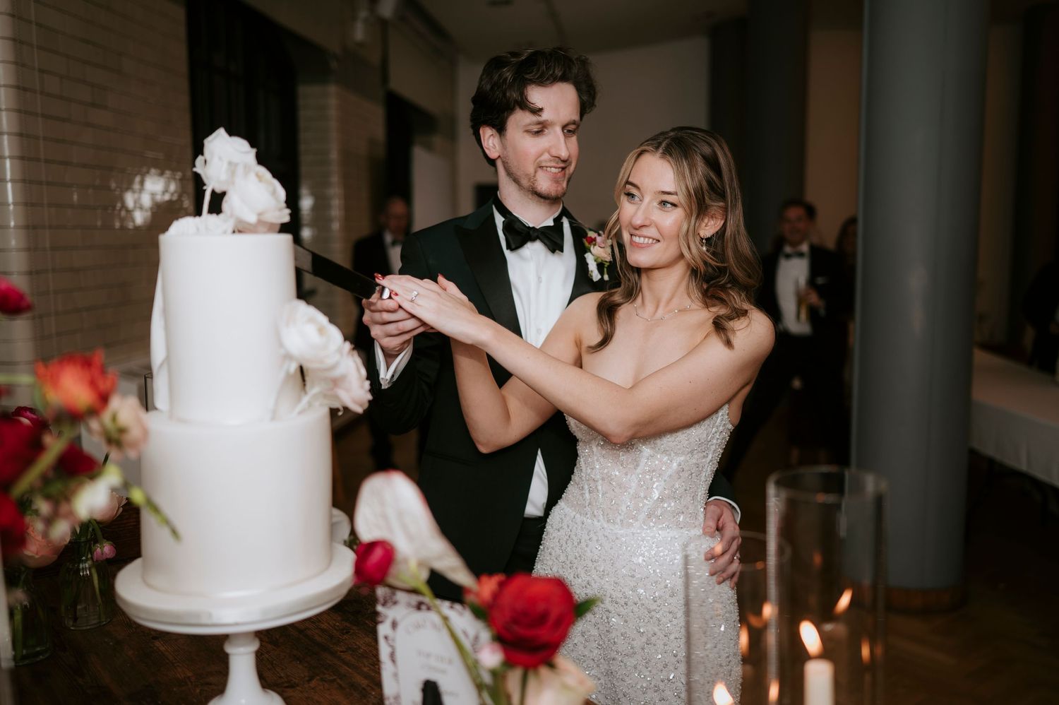 Wedding guests dancing and celebrating at an elegant indoor reception with white decor and candlelight.