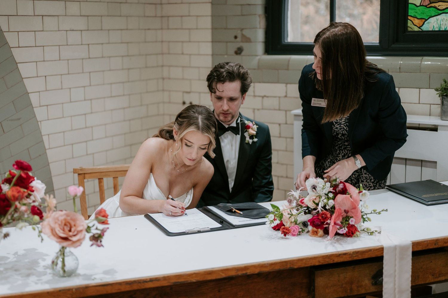 Wedding reception venue features white brick walls, wooden chairs and elegant floral centerpieces.