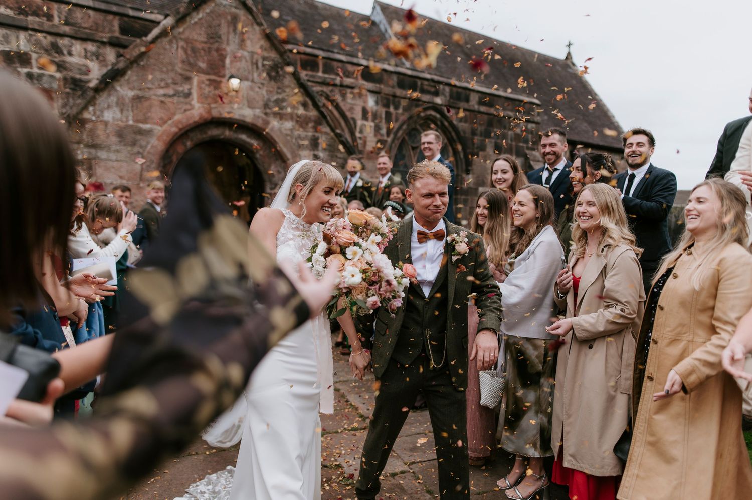 Wedding guests throw confetti at a joyful celebration outside a historic stone church.