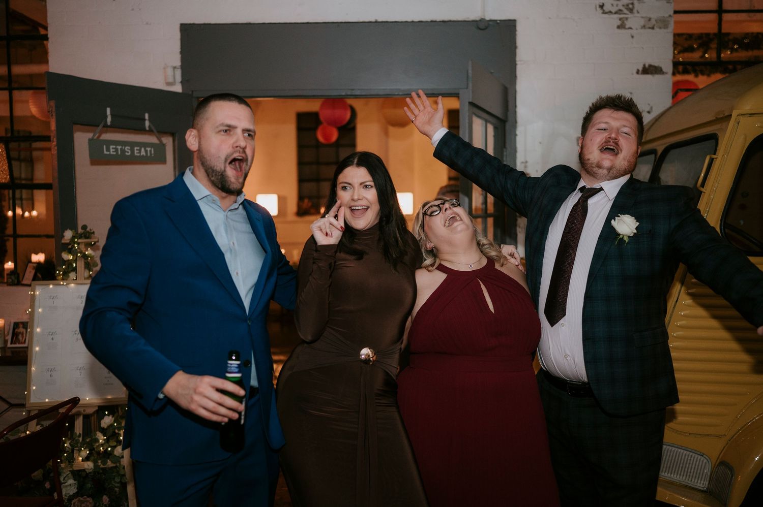 Four wedding guests laugh and celebrate energetically at a lively wedding reception venue.