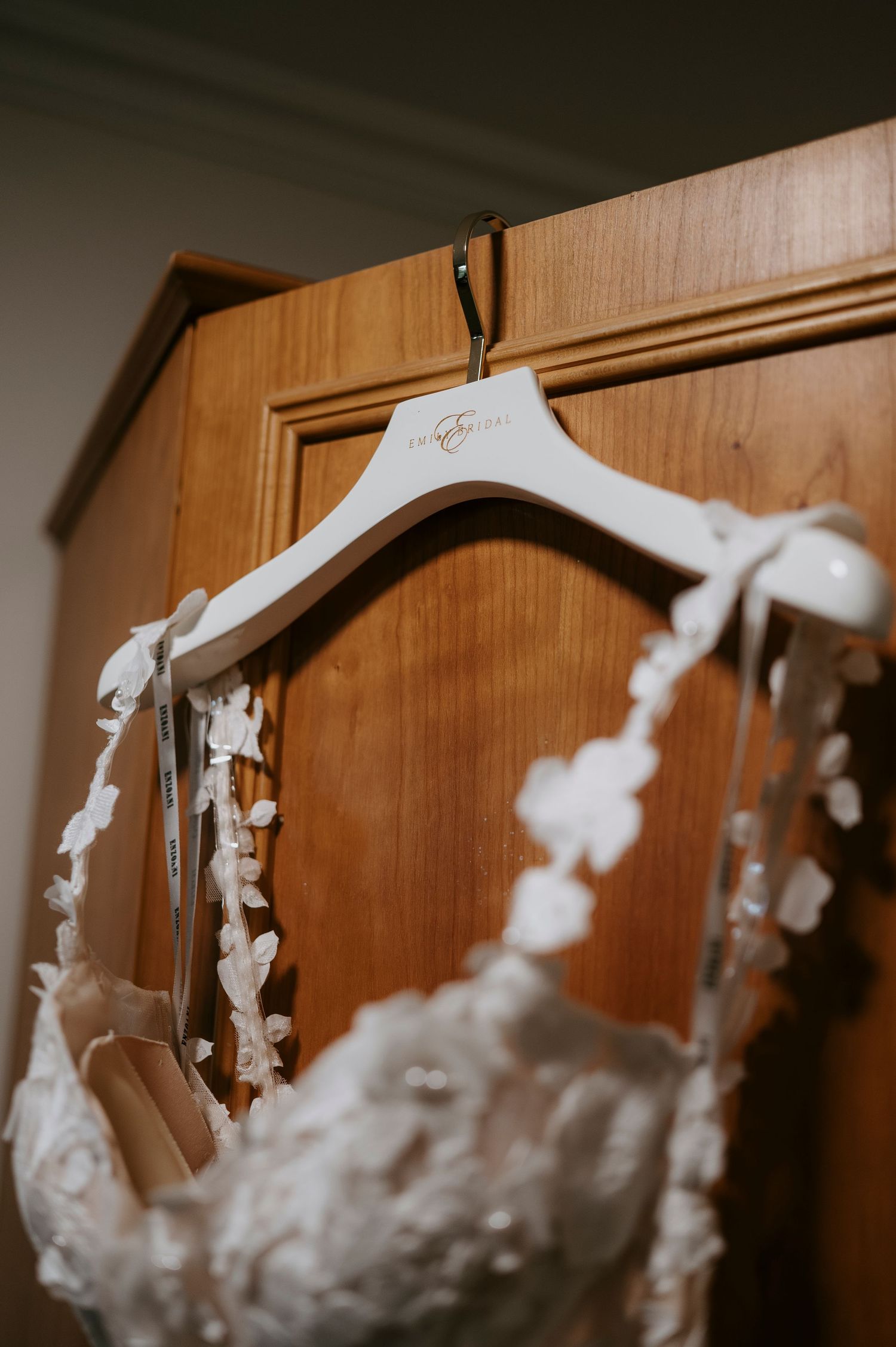 White floral wedding dress hanging on personalized bridal hanger on wooden wardrobe.