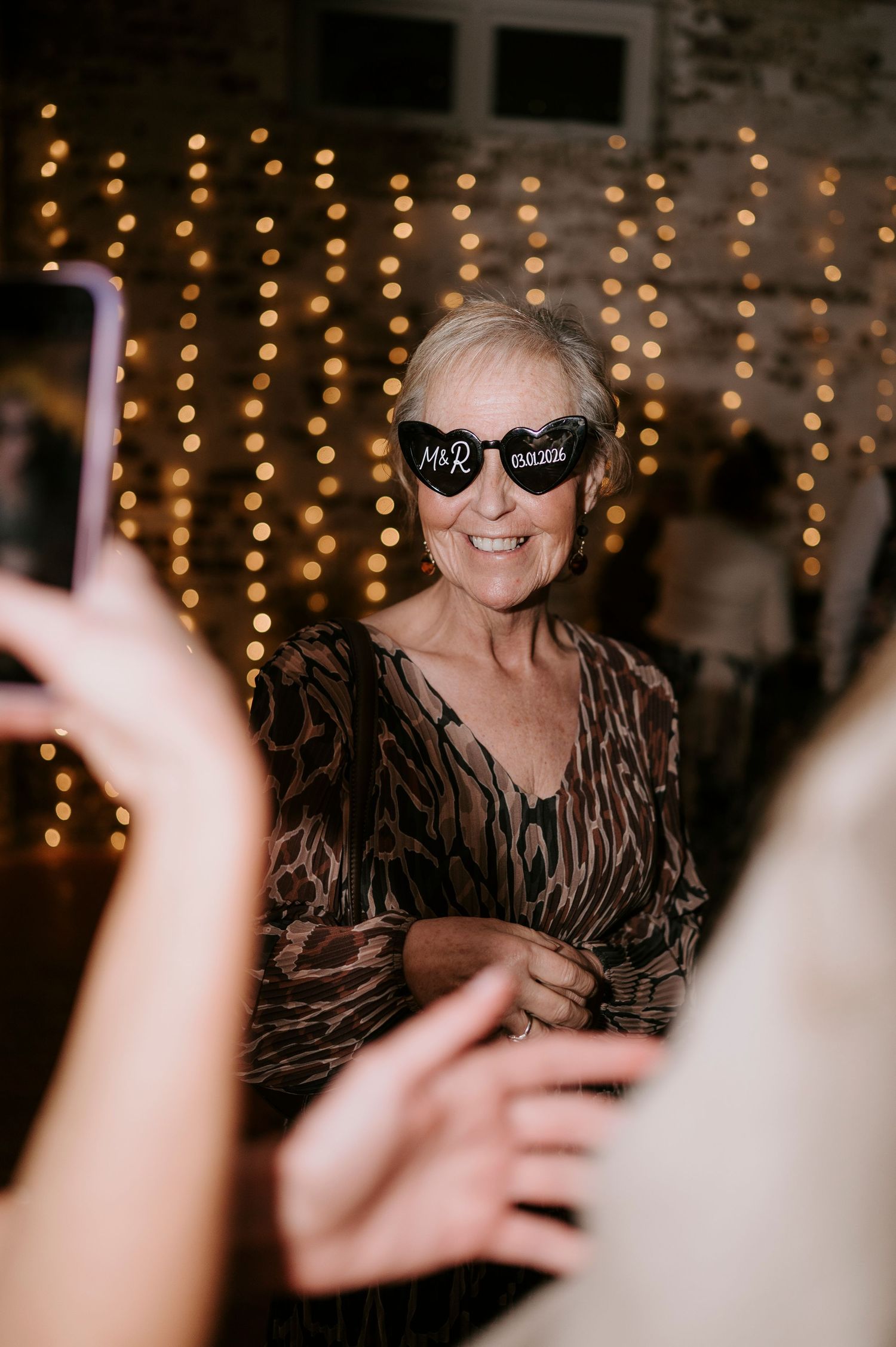 Smiling older woman wearing Mr & Mrs novelty sunglasses at the wedding reception dance floor.