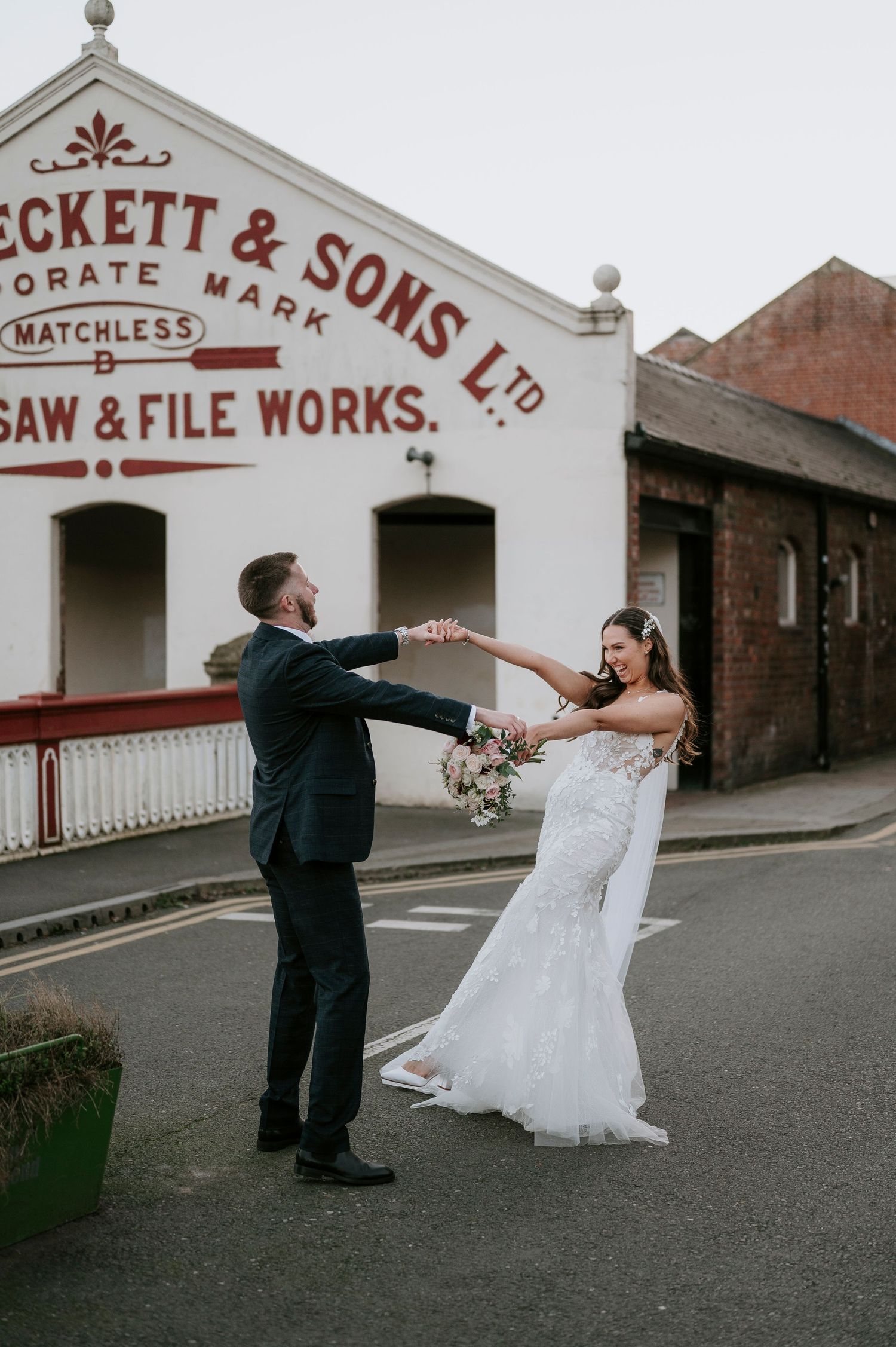 Bride and groom dance joyfully outside the historic Beckett & Sons Ltd building on their wedding day.