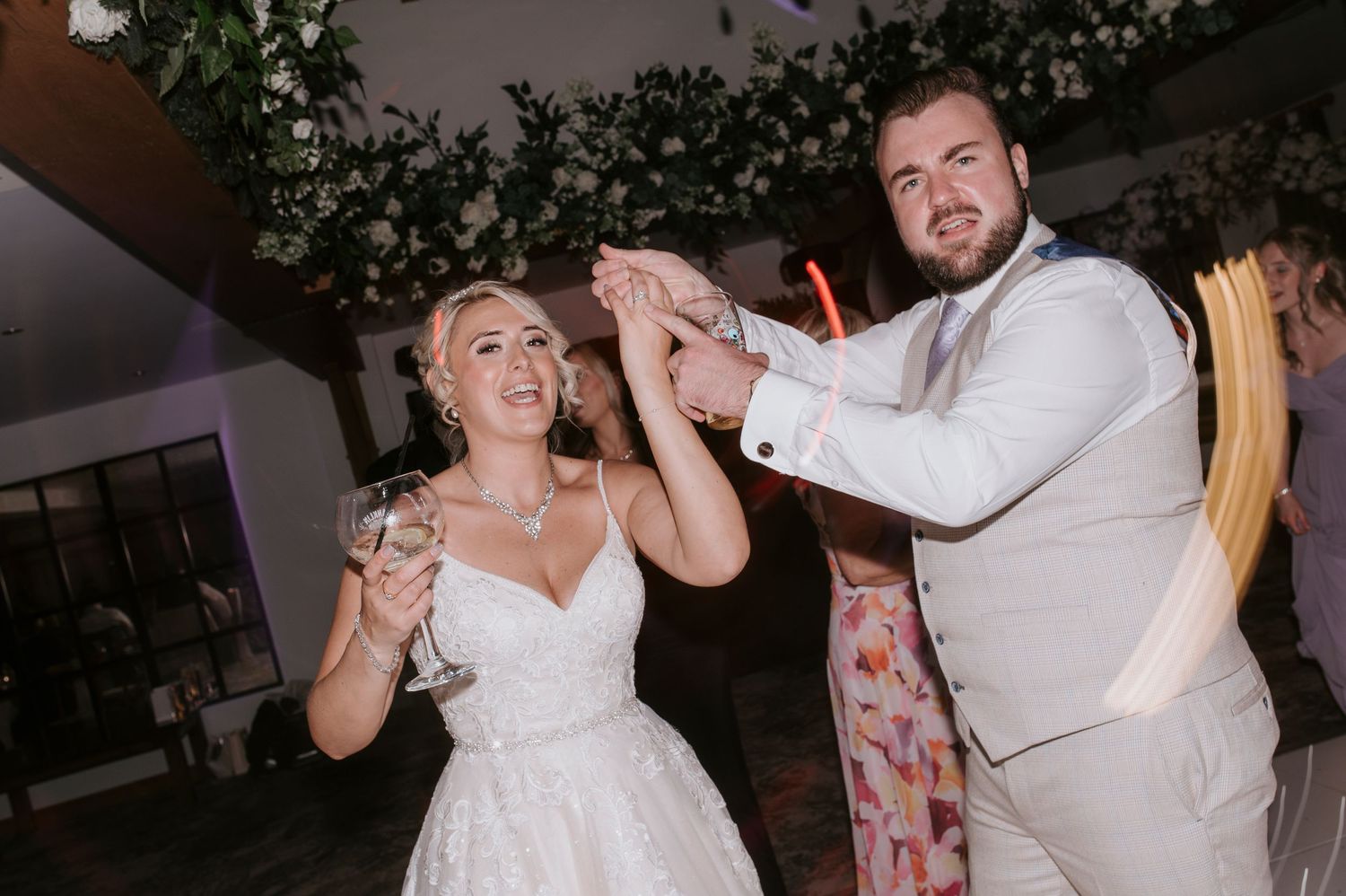 Wedding guests dance and celebrate together on a dimly lit dance floor at an evening reception.