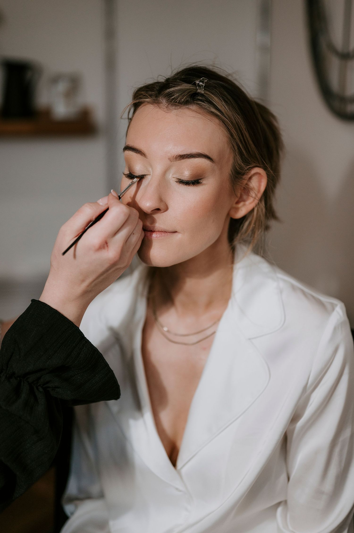 Makeup artist applying eye makeup to model wearing white blazer during bridal preparation.