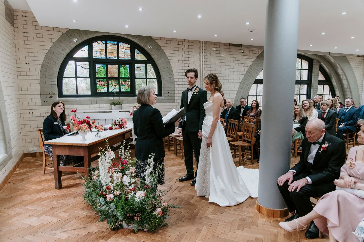 Wedding ceremony guests seated in elegant church with brick walls and arched windows.