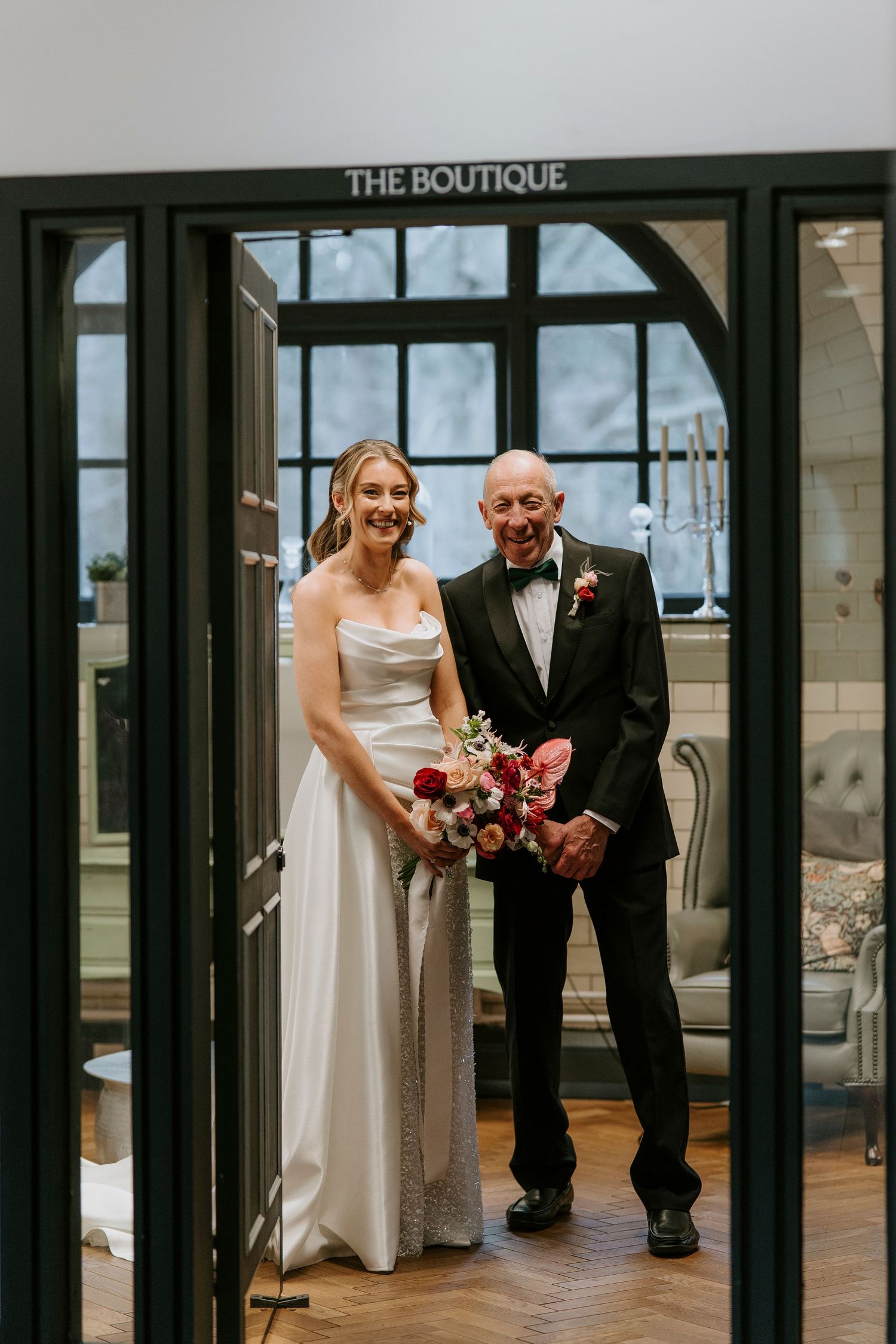 Wedding party members in formal attire gather outside a boutique entrance with elegant floral bouquets.