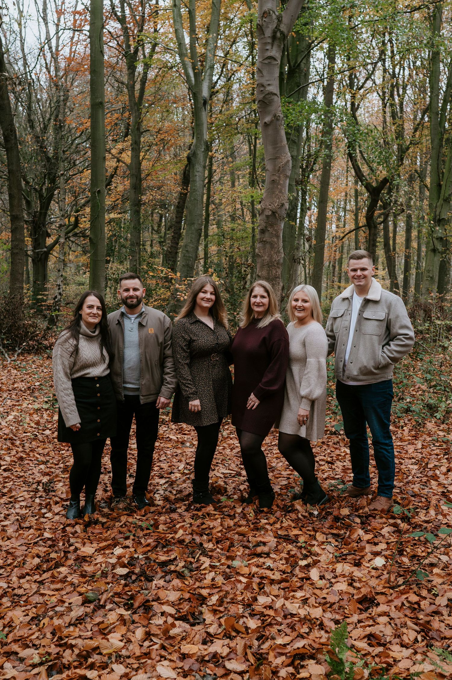 A group of people standing together in an autumn forest with fallen leaves covering the ground.